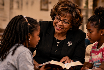 An older woman reading a book to two young girls in a cozy indoor setting.