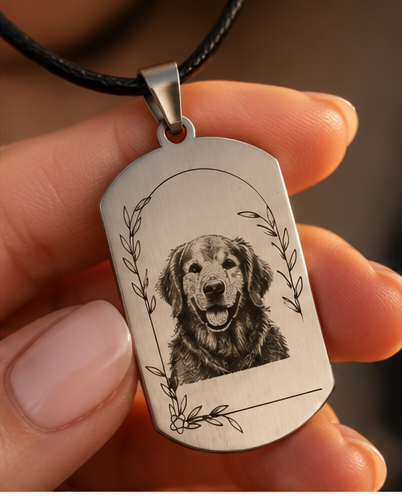 A metal dog tag pendant with an engraved image of a smiling retriever puppy, held by a person's fingers.