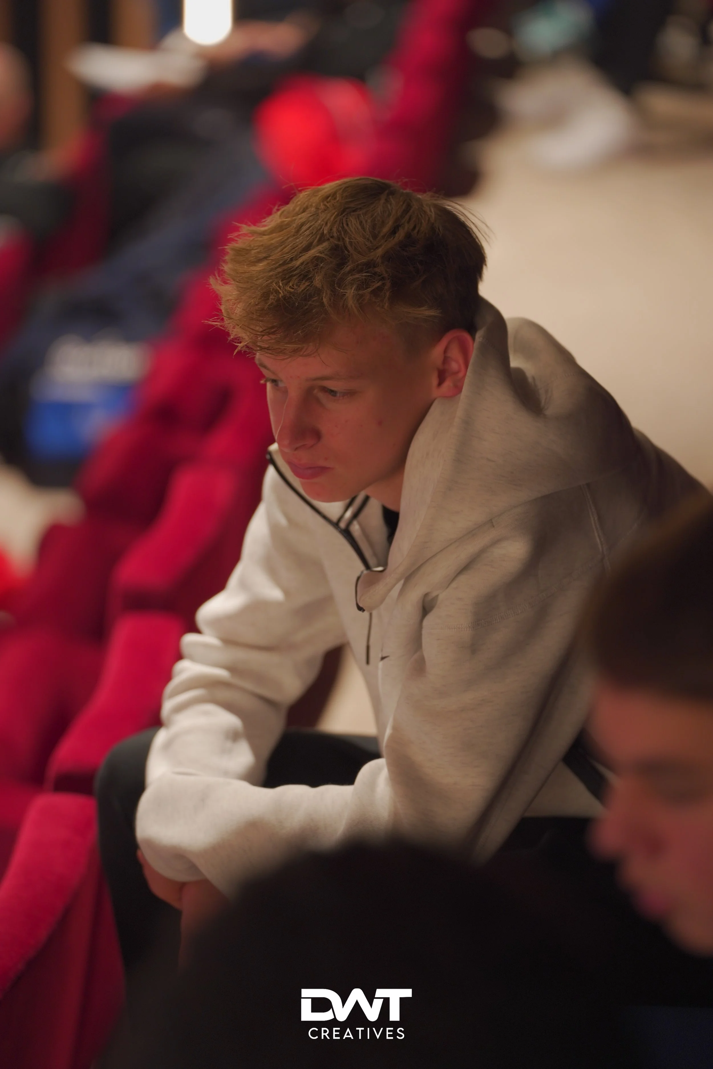 Jongen in witte hoodie in een theater met rode stoelen.