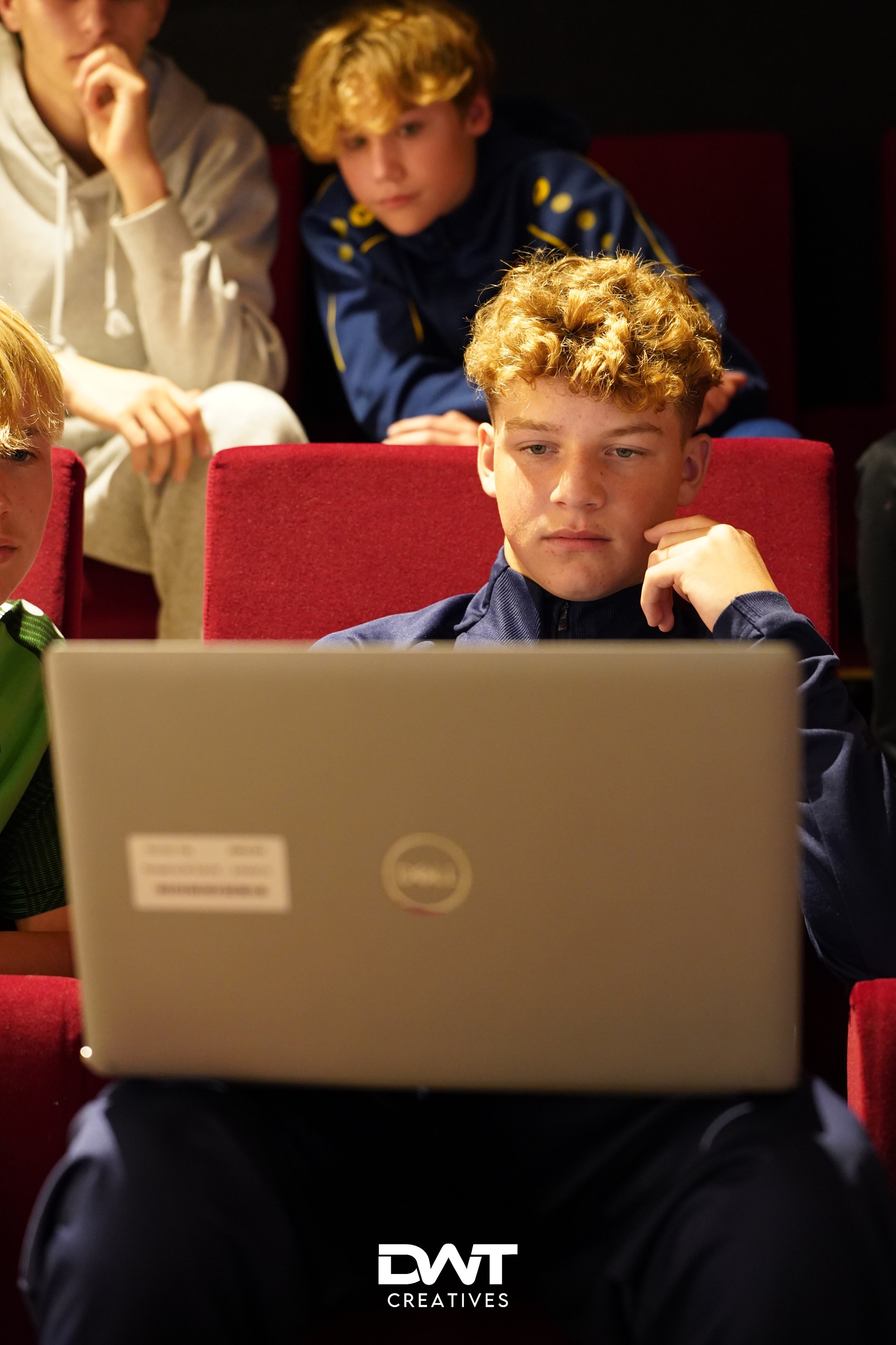 Jongens kijken naar een laptop in een theaterachtige omgeving.