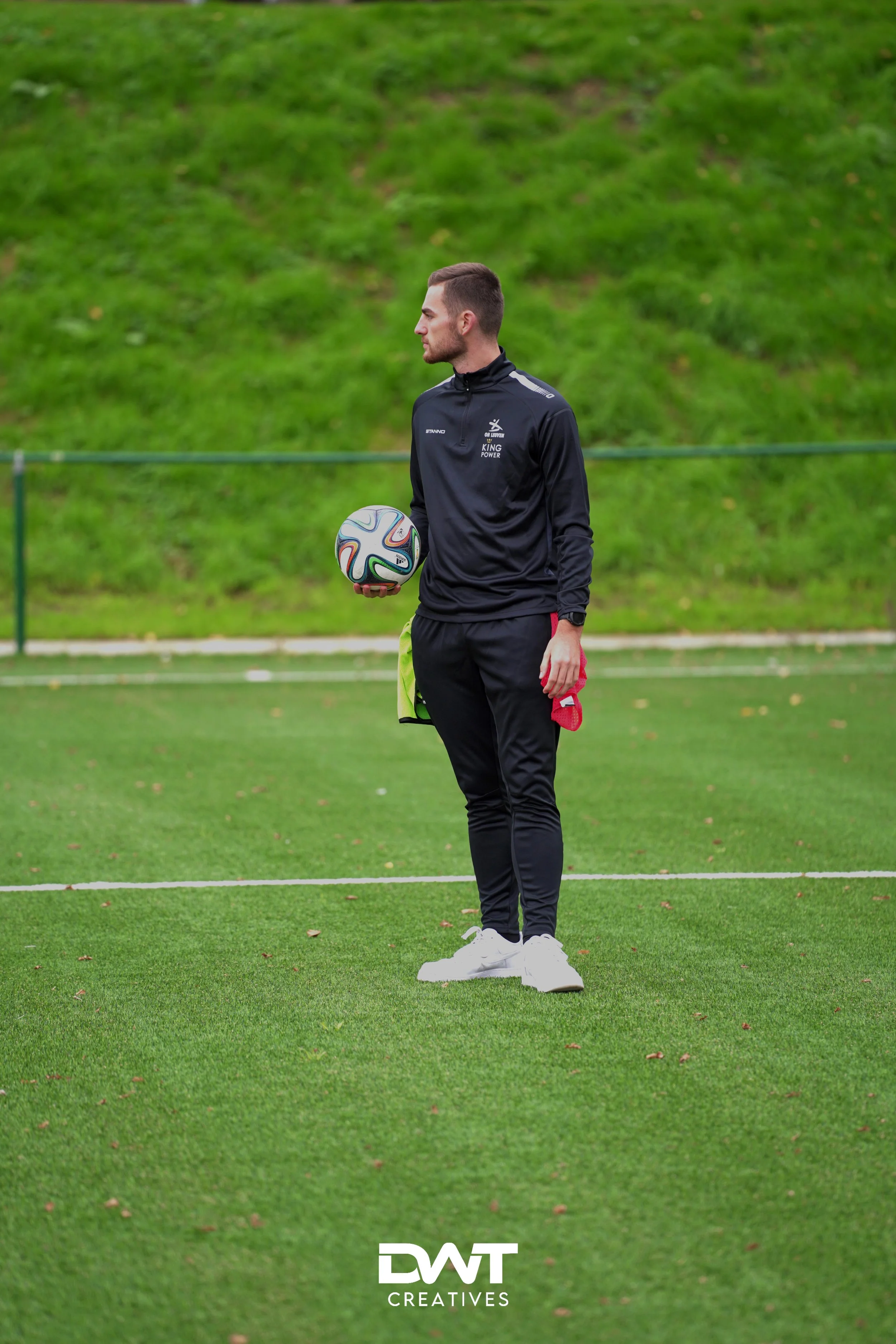 Man op voetbalveld met bal en sportoutfit, gras op de achtergrond.
