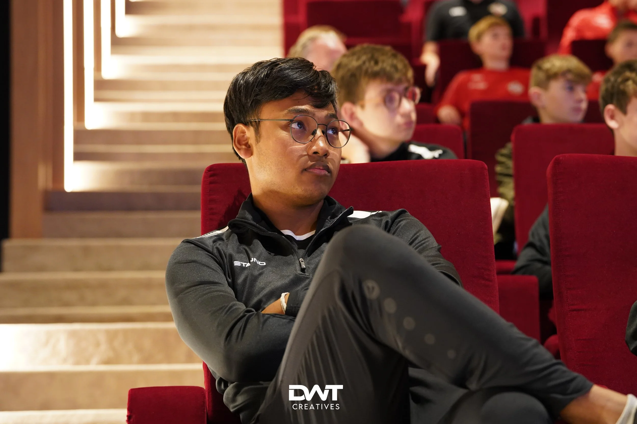 Mensen in een auditorium met rode stoelen.