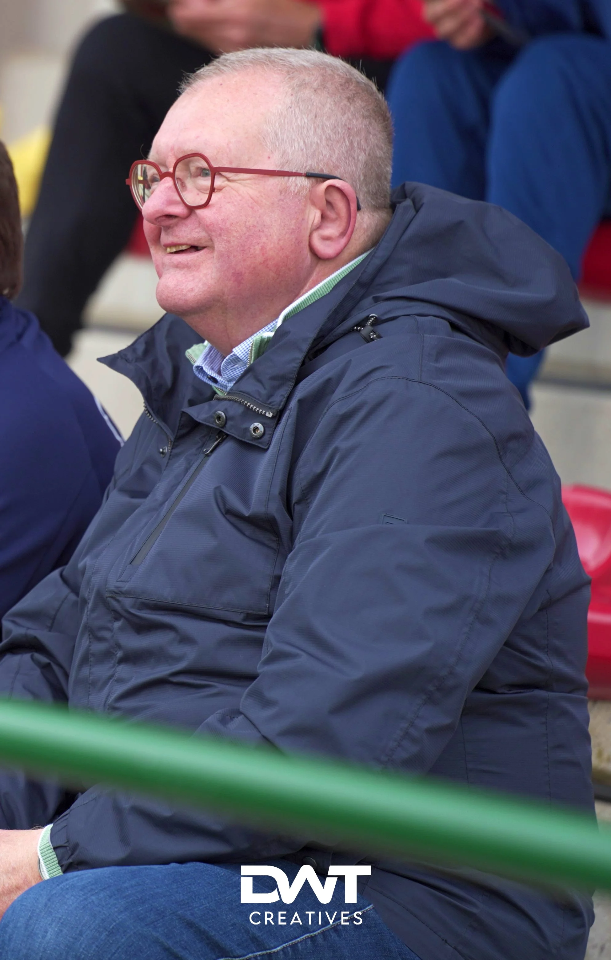 Man met bril en jas zit op tribune