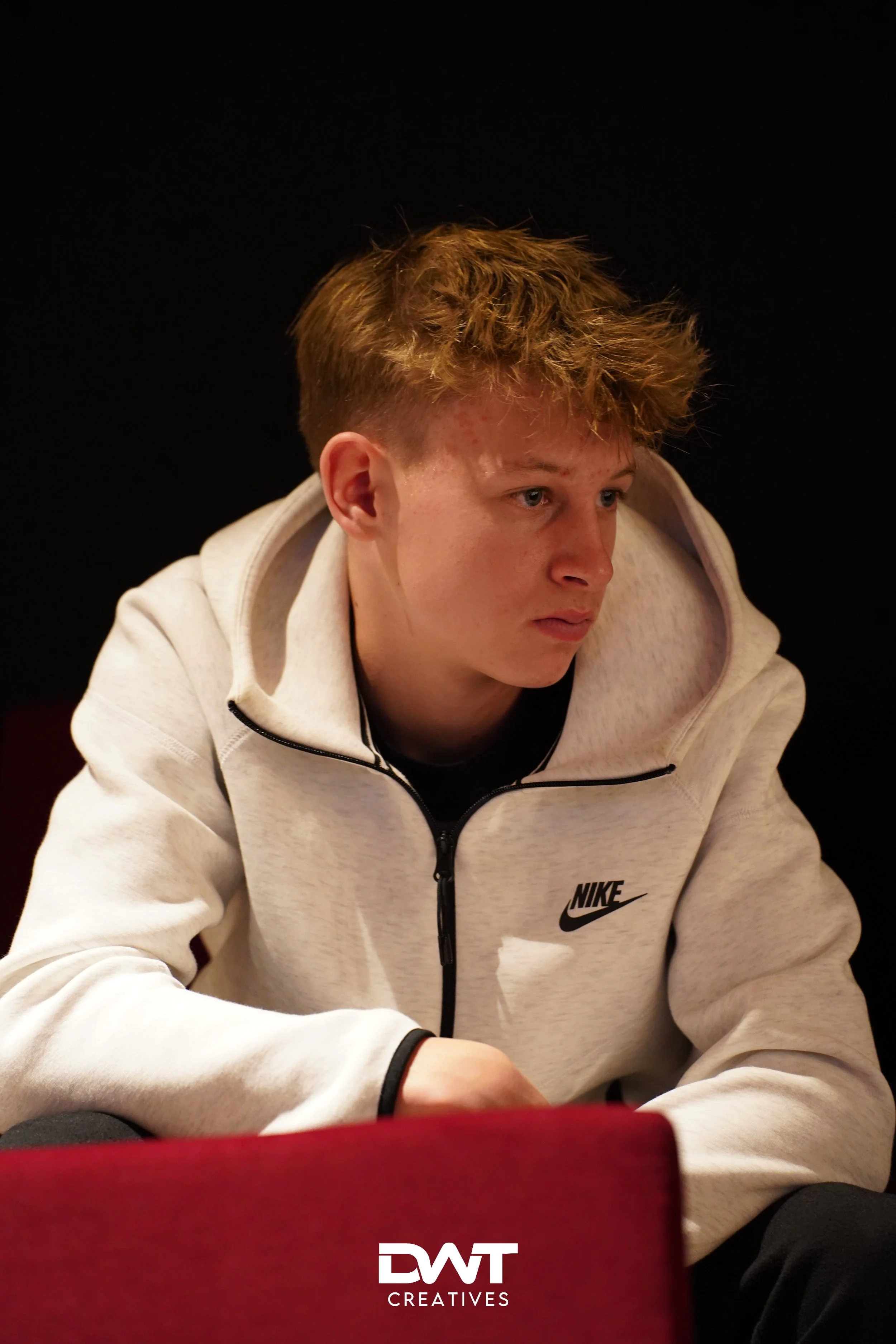 Persoon in witte Nike-hoodie tegen zwarte achtergrond.