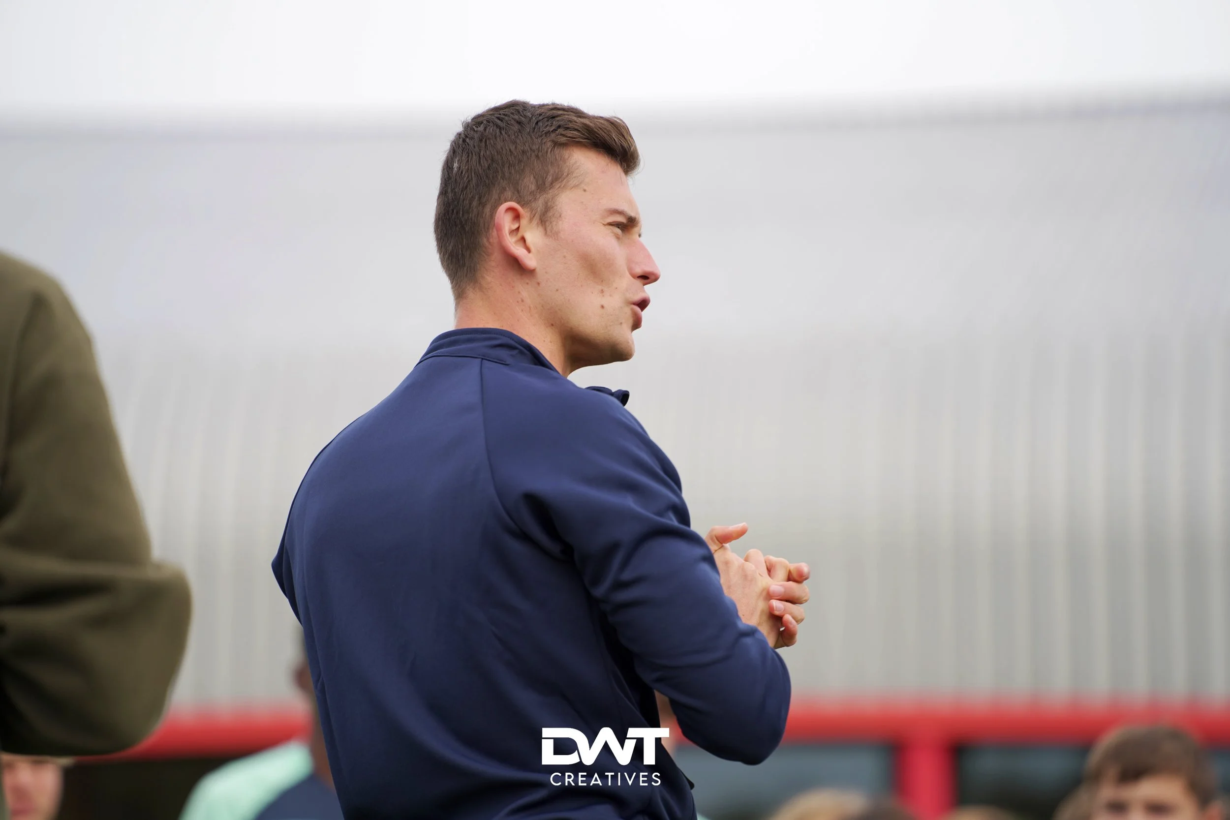 Een man in een blauwe jas spreekt buiten voor een groep mensen.