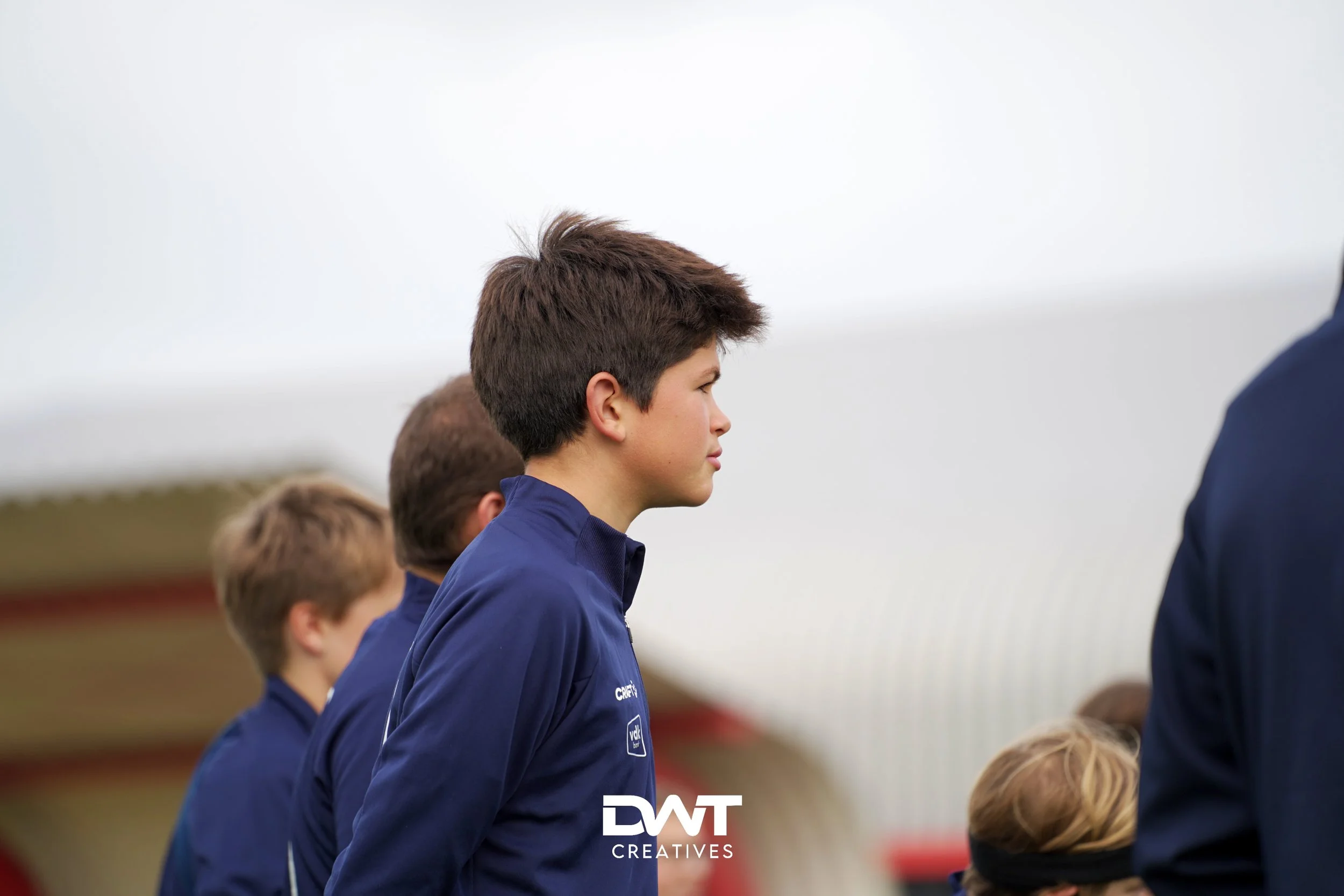 Groep jongens in blauwe sportkleding, buiten op een sportlocatie.