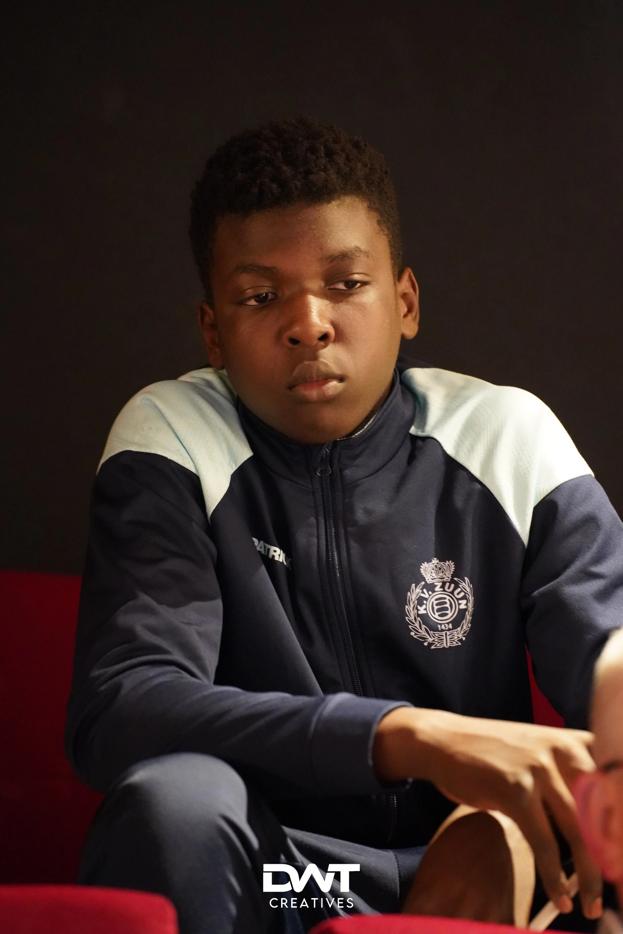 Jongen zit in een donker trainingspak met embleem.