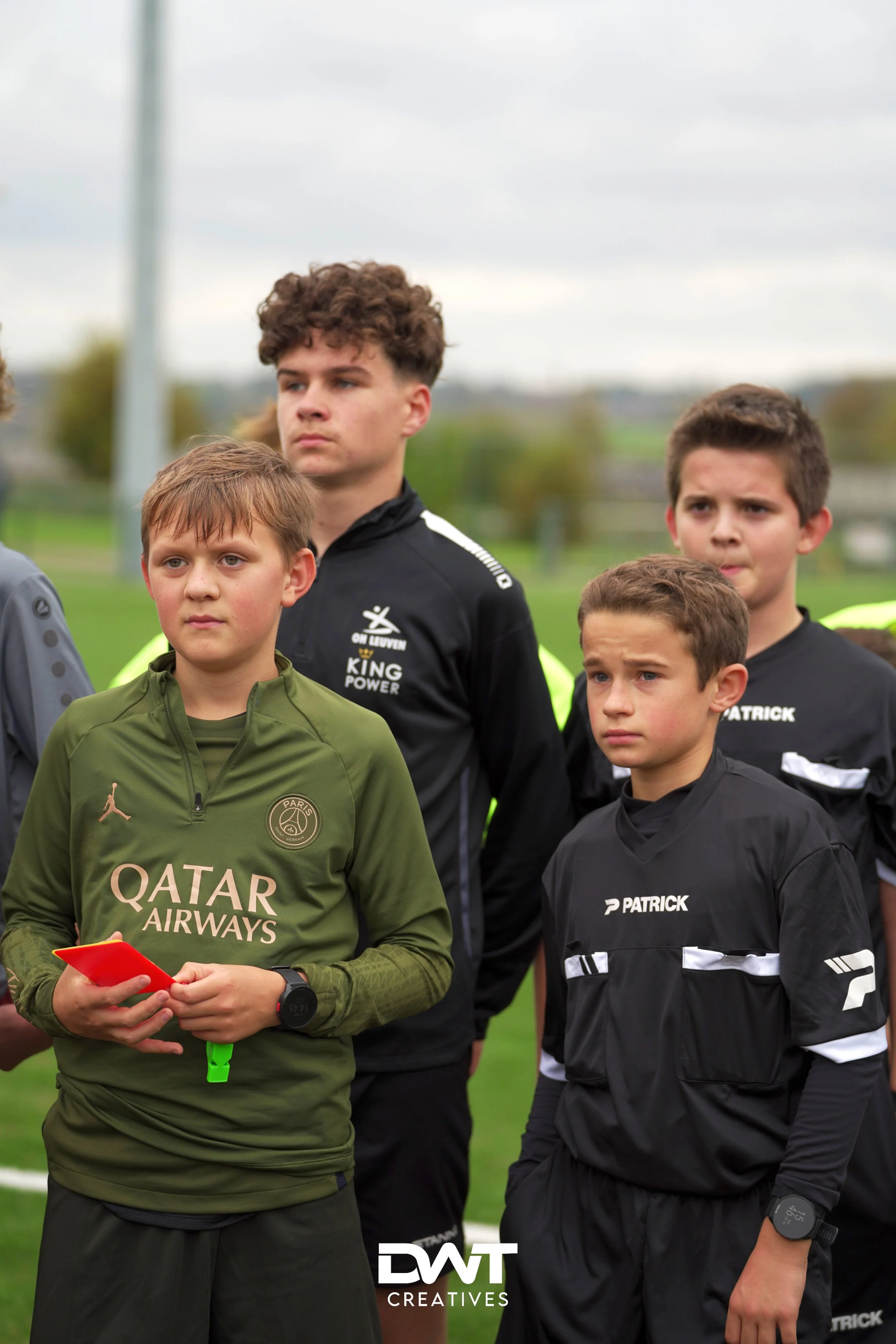 Jonge voetballers in sportkleding staan op een grasveld. Een van hen houdt een rode kaart vast.