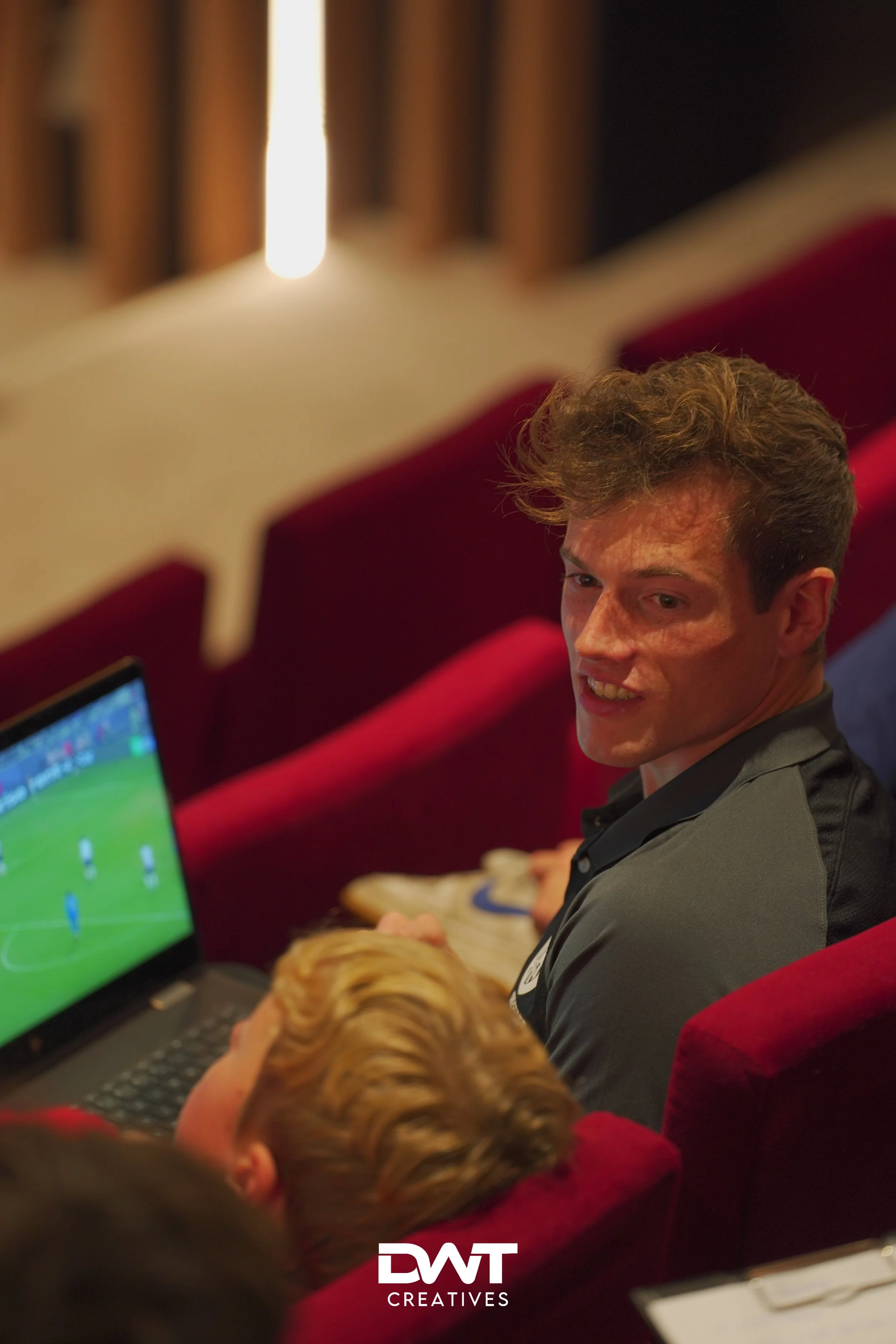 Man in rood theaterstoel kijkt naar laptop met voetbalwedstrijd.