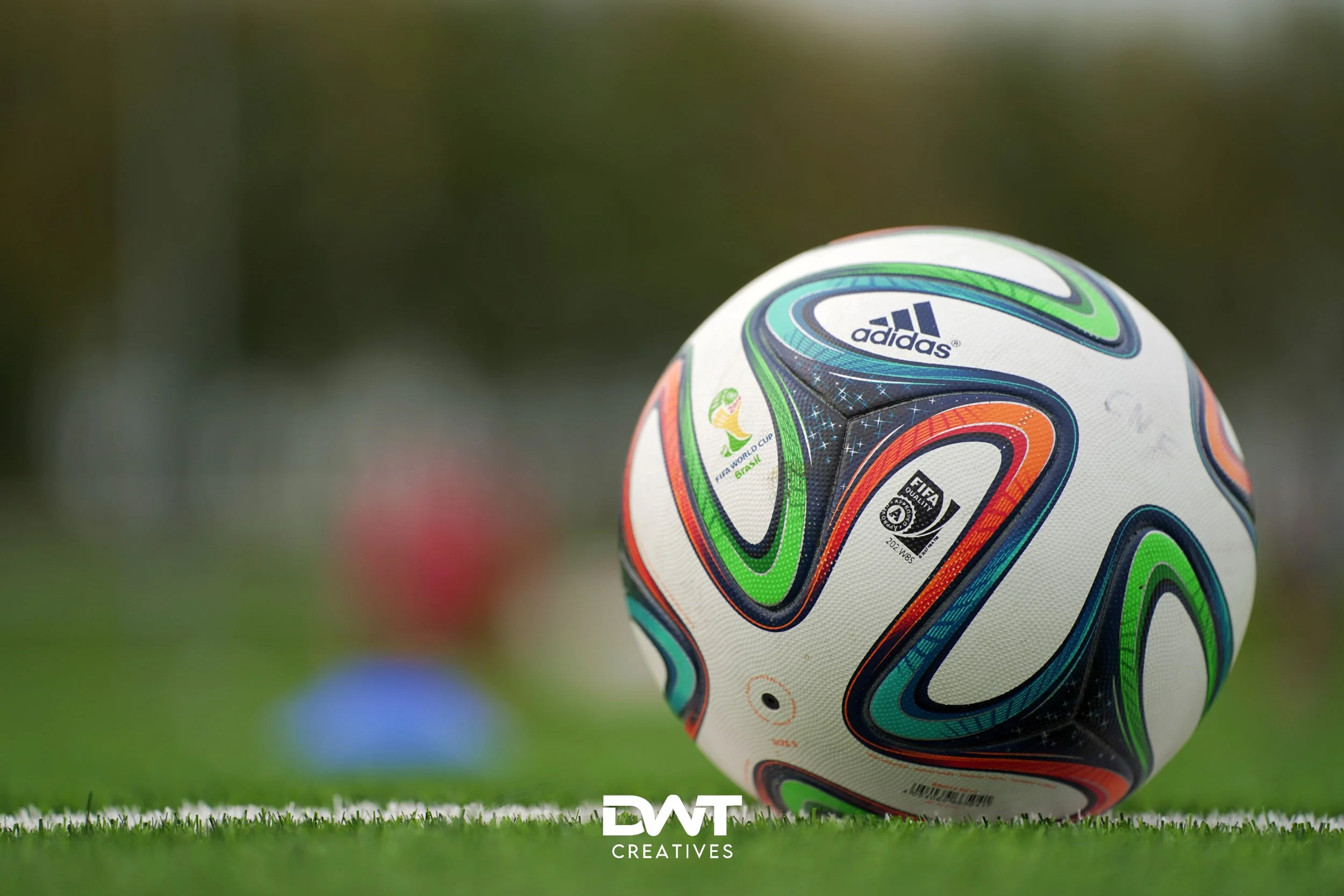 Voetbal met veelkleurig patroon op grasveld, logo van Adidas en FIFA Wereldbeker zichtbaar.