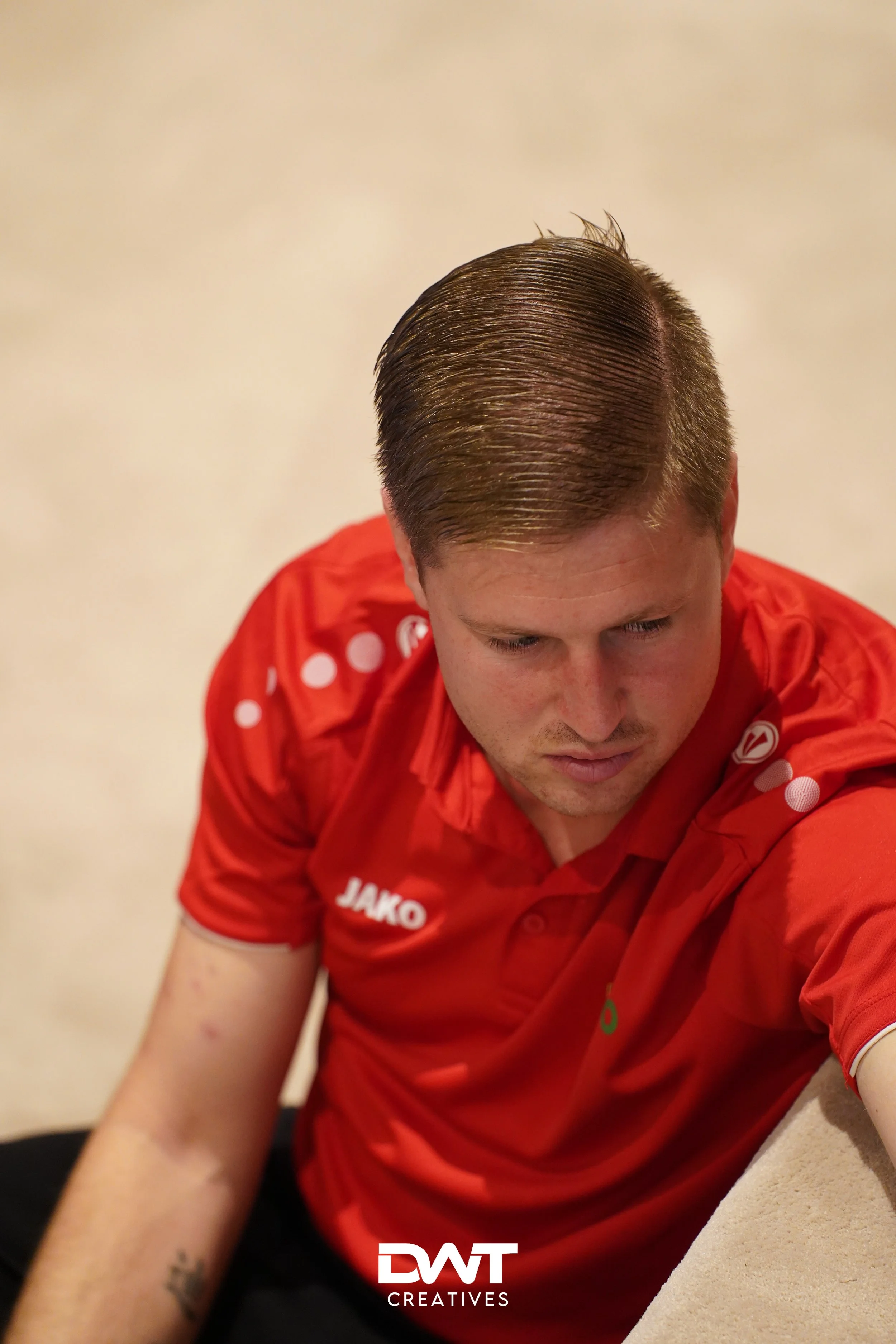 Man in rood Jako-shirt kijkt naar beneden, met een lichtgevende achtergrond.