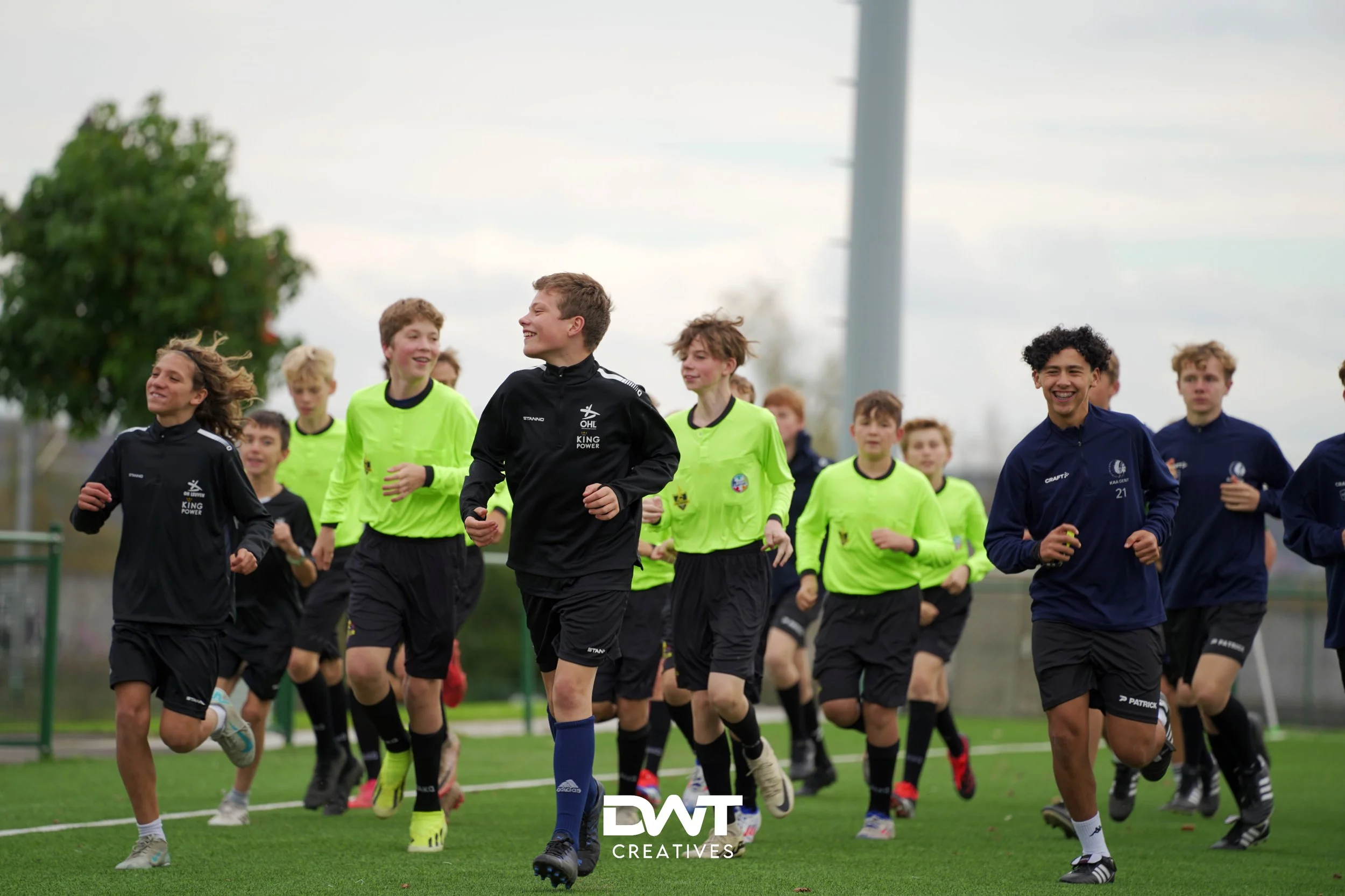 Jonge voetballers rennen op een veld tijdens een training. Ze dragen zwarte en felgroene sportkleding.