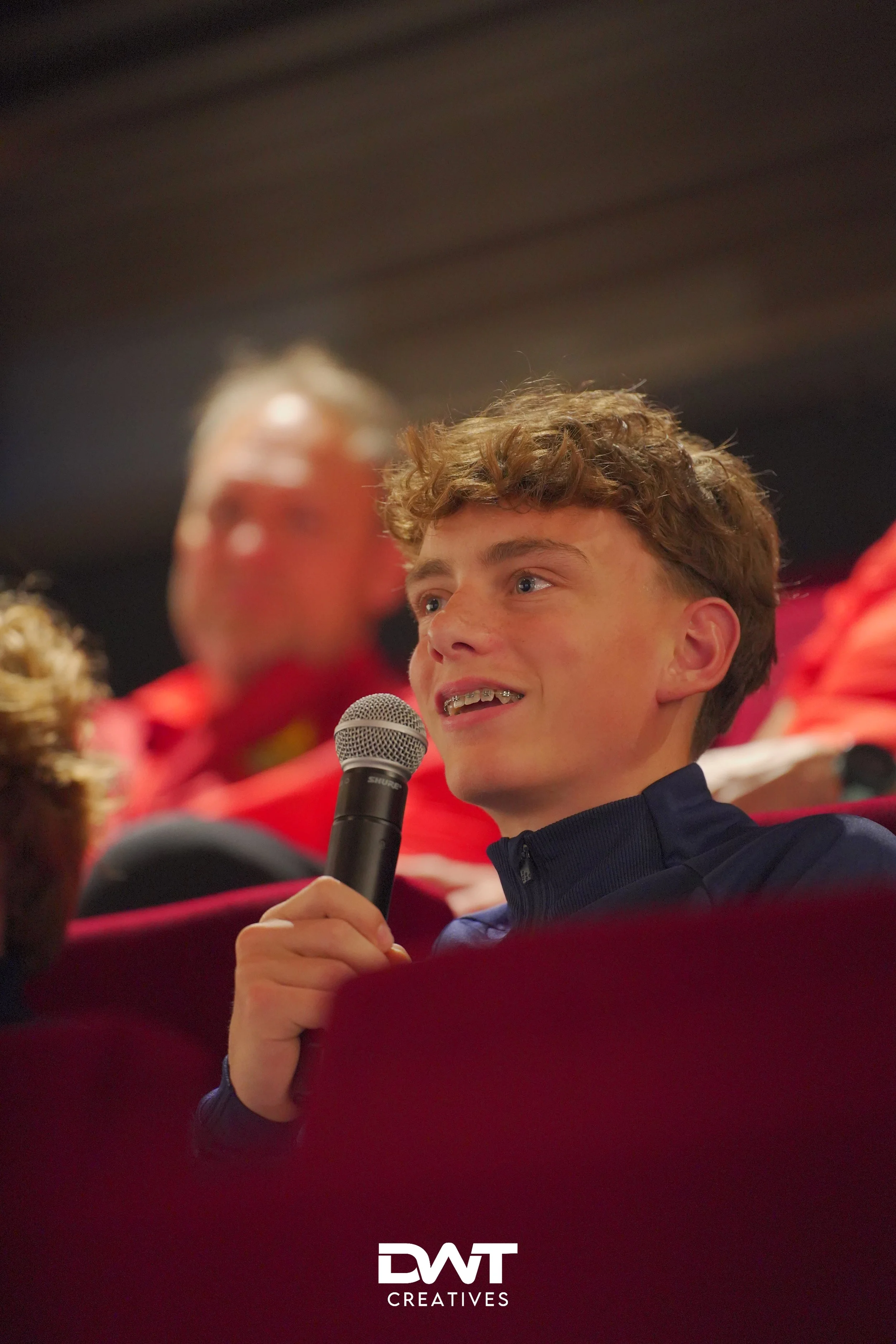 Jongeman met microfoon tijdens een evenement in zaalomgeving.