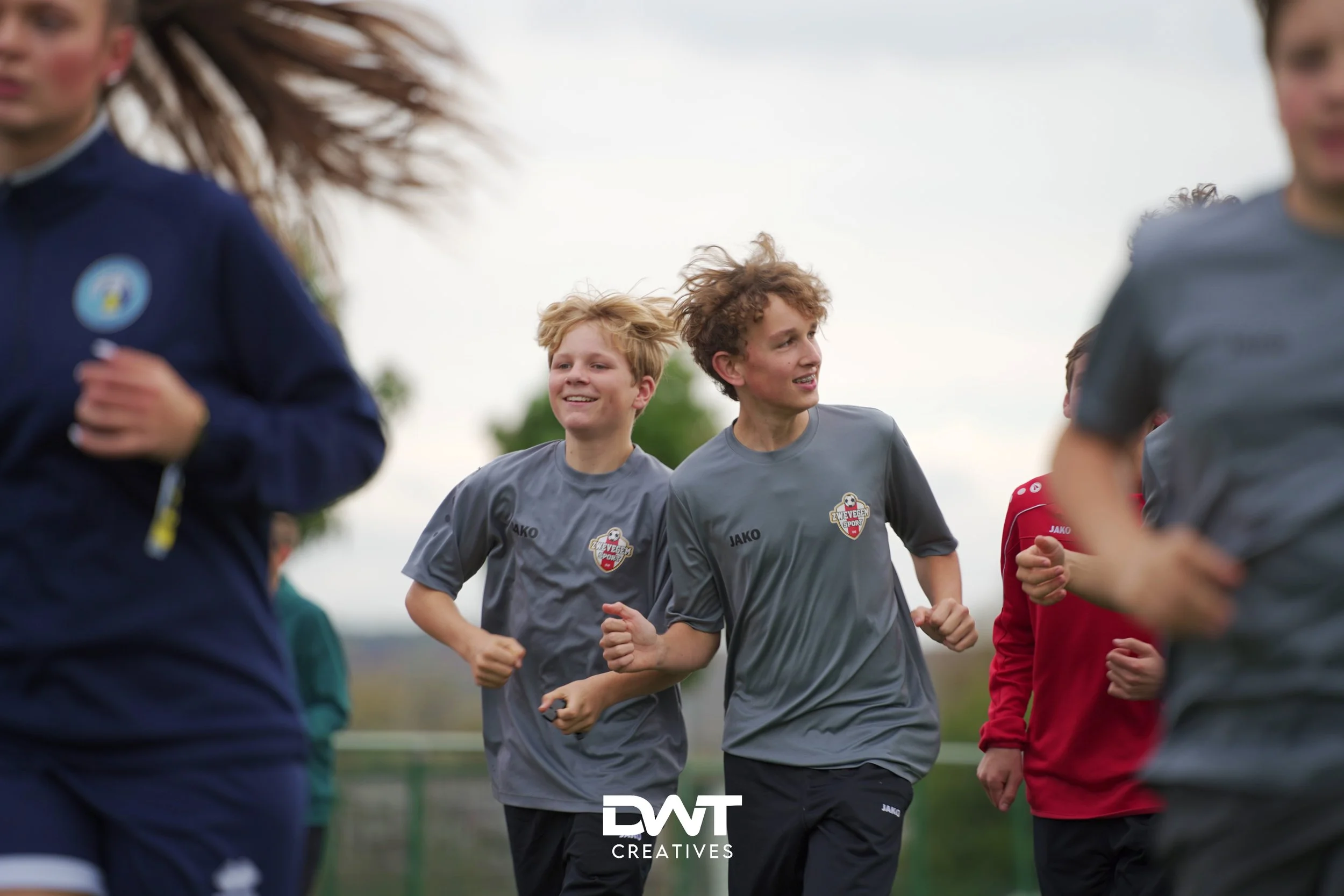 Jonge voetballers in grijze sportkleding rennen buiten tijdens een training of warming-up.