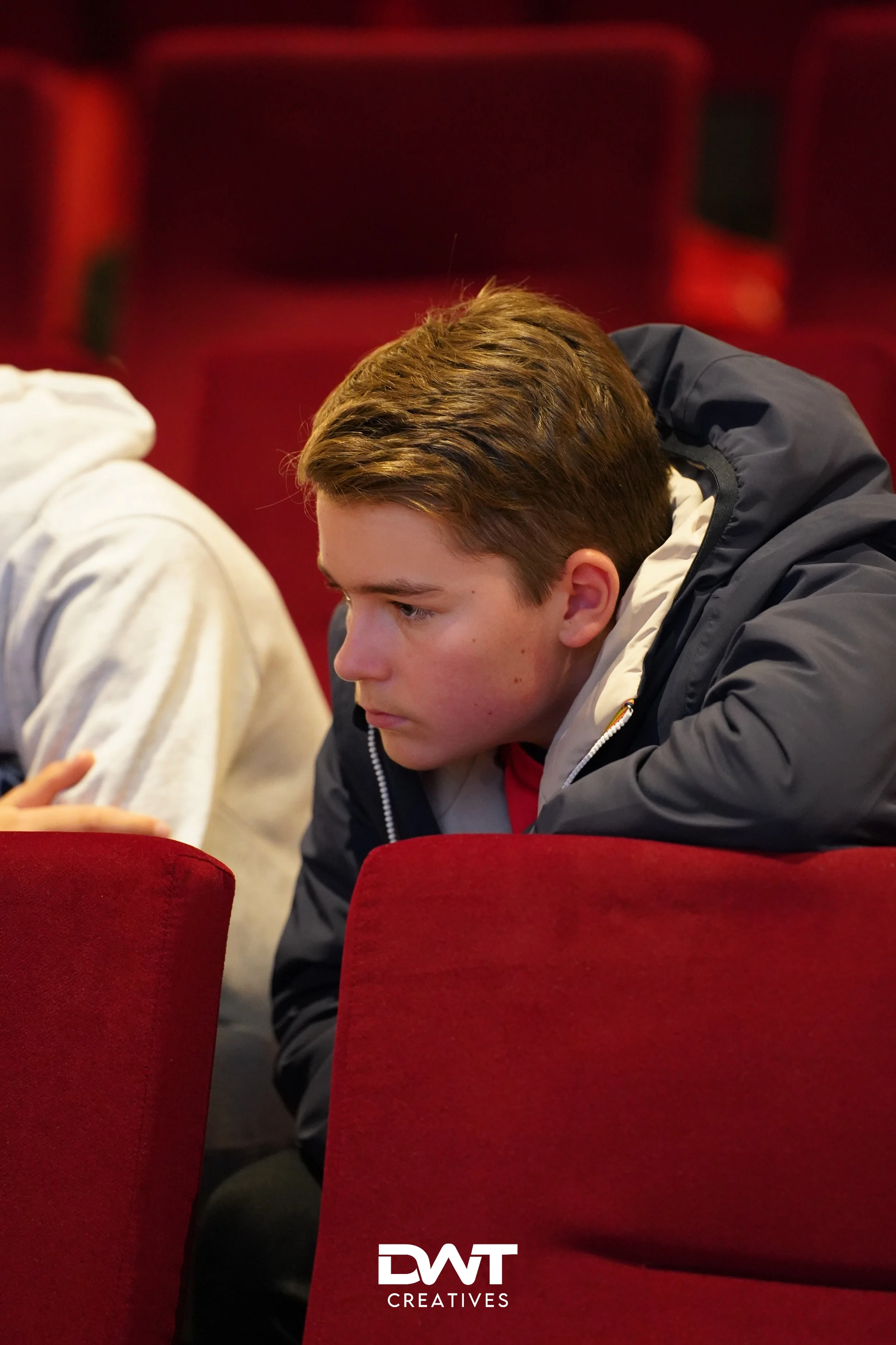 Jongen verdiept in gedachte terwijl hij in een rode bioscoopstoel zit.