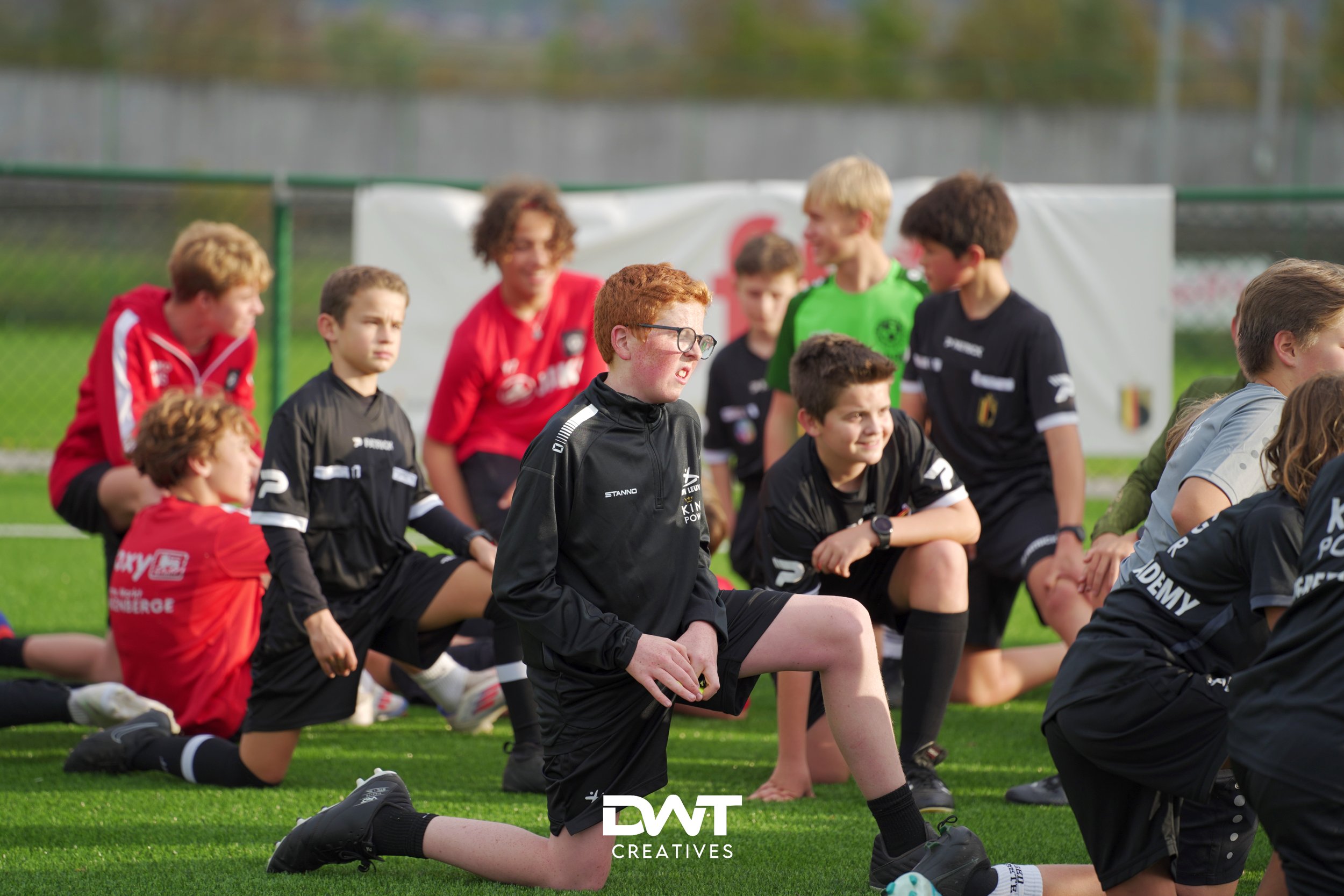 Kinderen in sportkleding doen kniebuigingen op een voetbalveld.