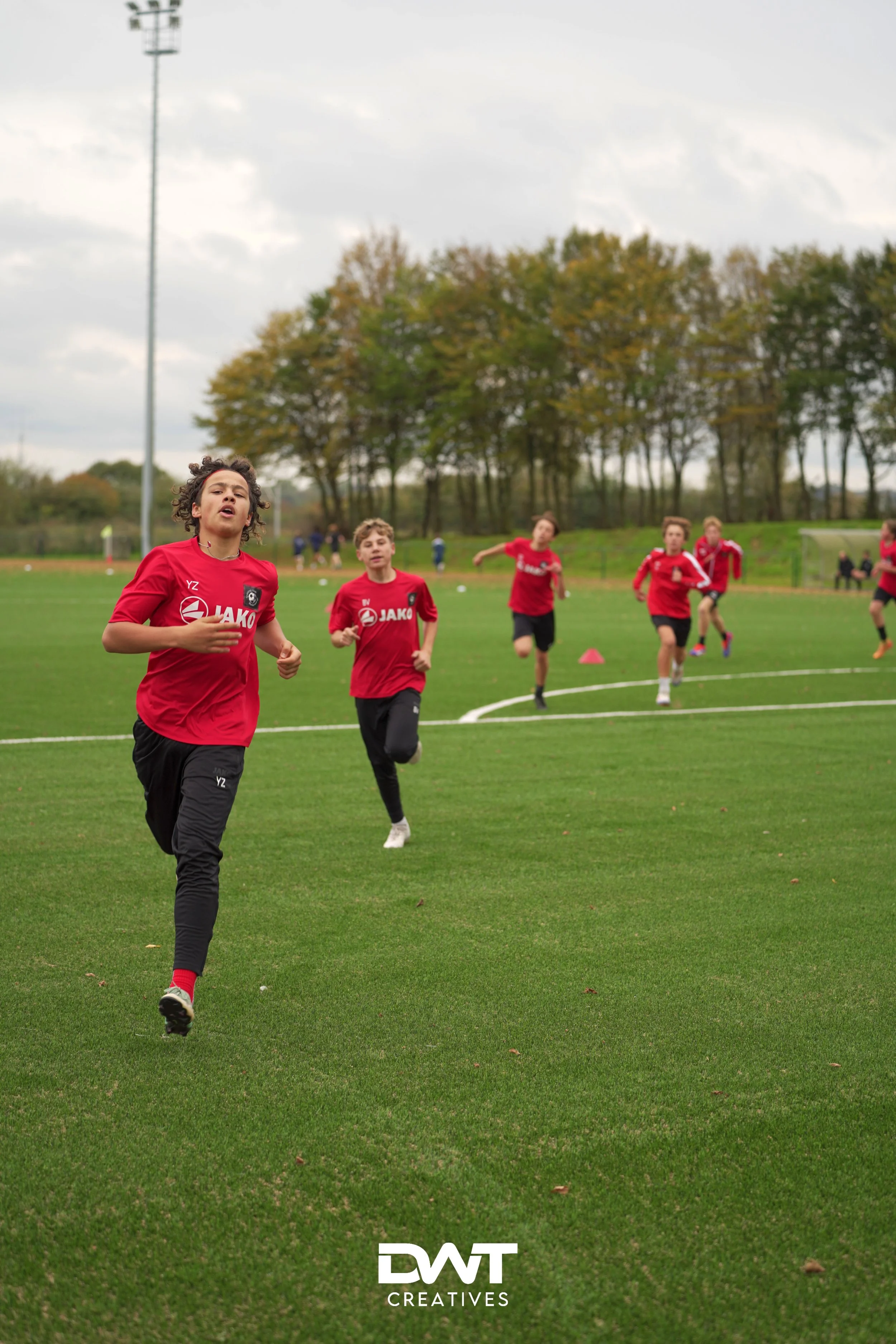 Jongens in rode sportkleding rennen op een grasveld tijdens een trainingssessie.