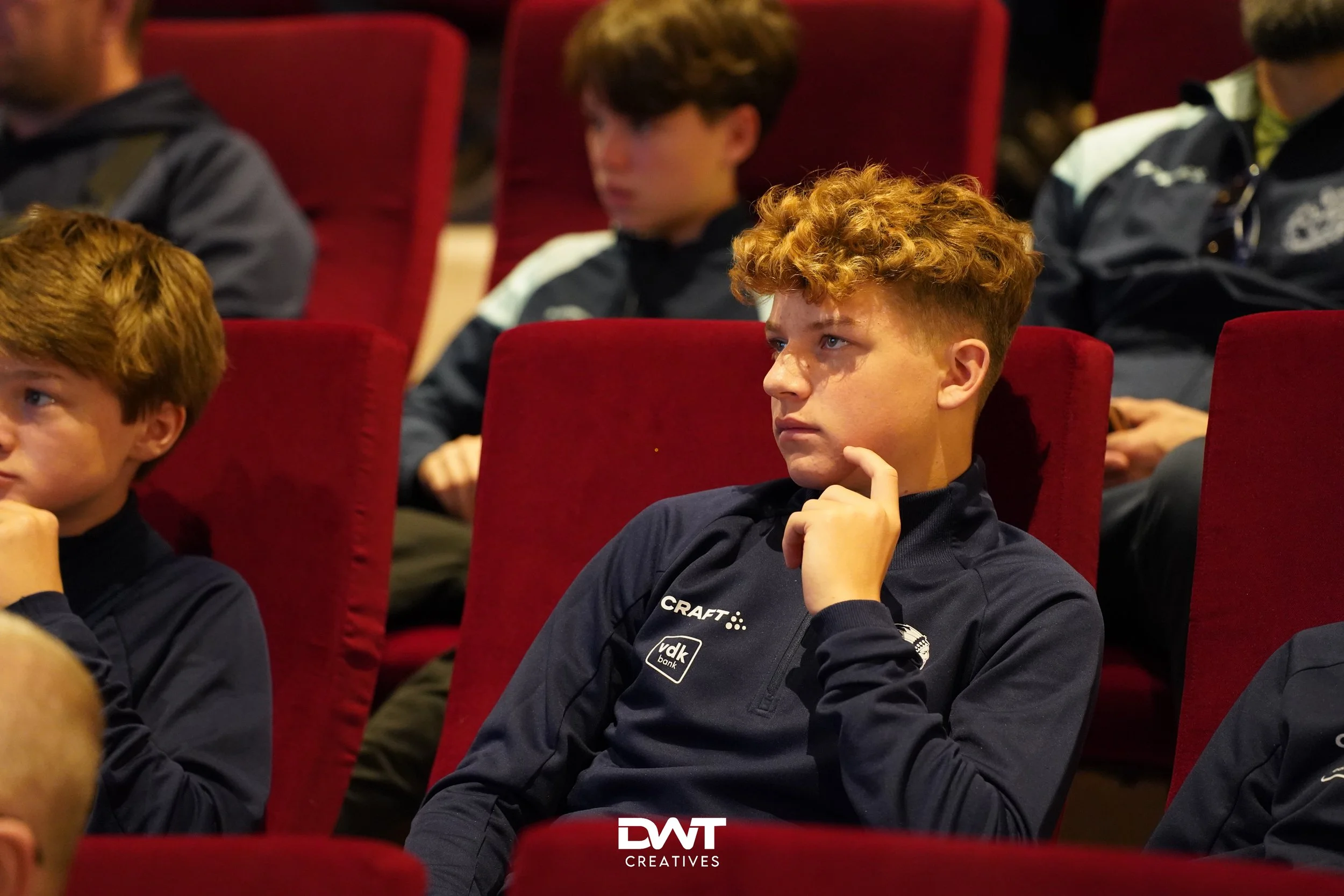 Jongen in rode bioscoopstoel, denkt na of luistert aandachtig.