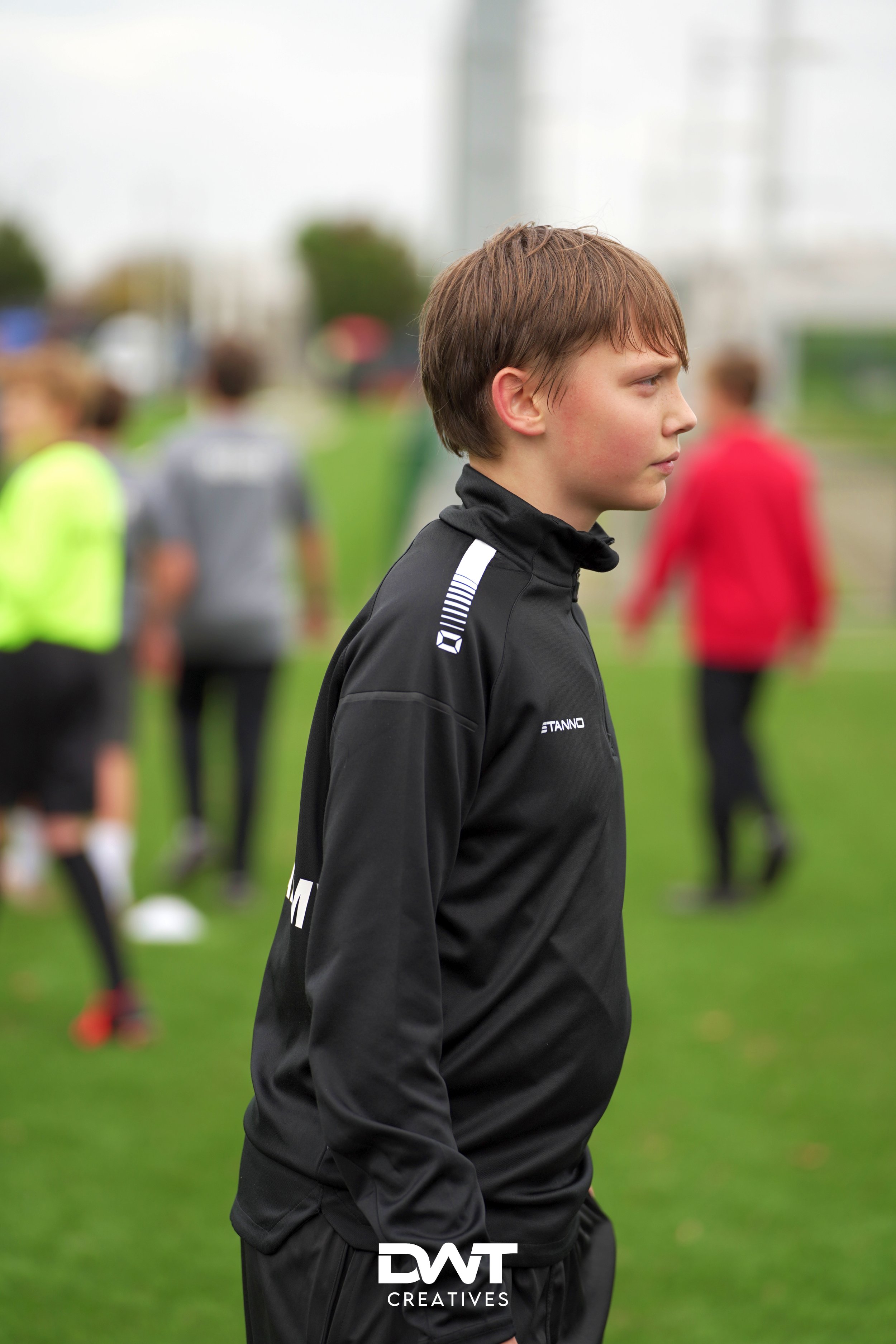 Jongen in sportkleding staat op een grasveld met andere mensen op de achtergrond.