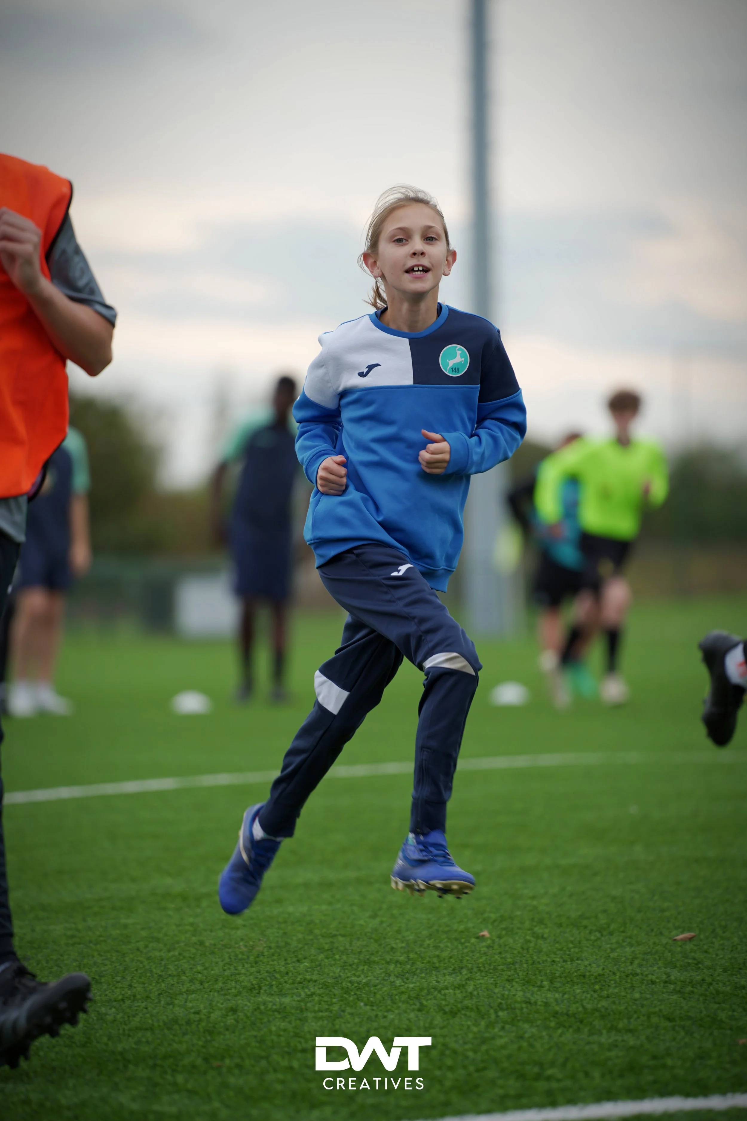 Kind in sportkleding rent op een voetbalveld tijdens een training, omringd door andere spelers.