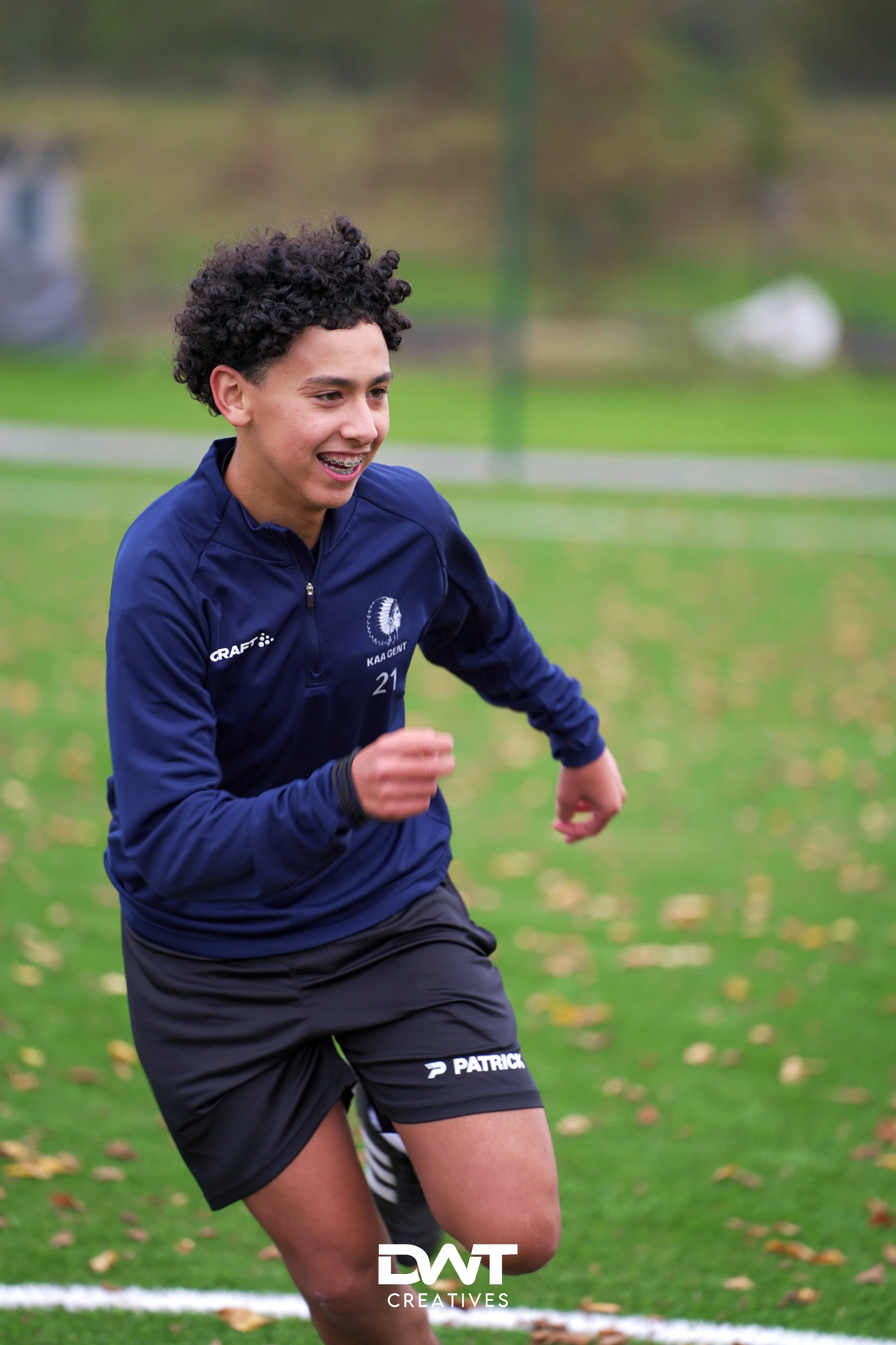 Jonge voetballer in sportkleding rent op een grasveld onder een bewolkte hemel.