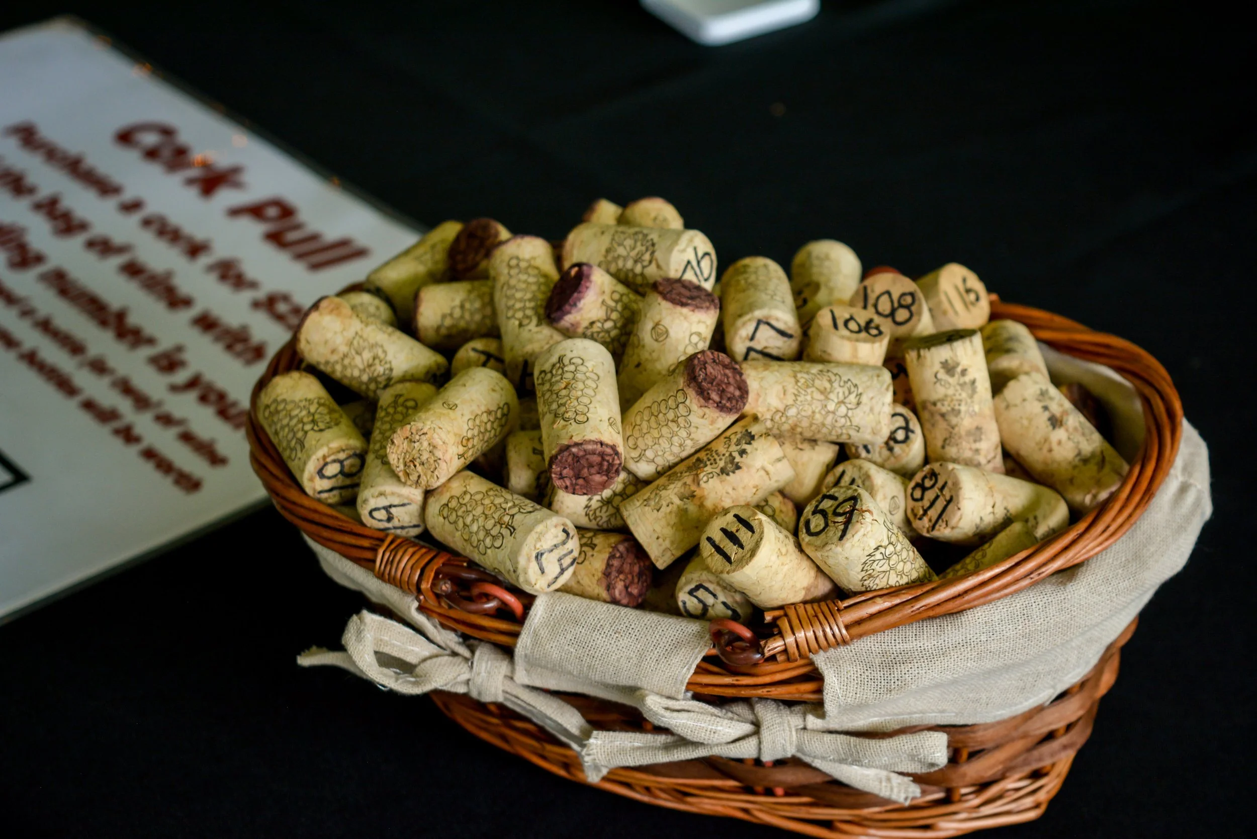 A wicker basket filled with used wine corks on a black surface.