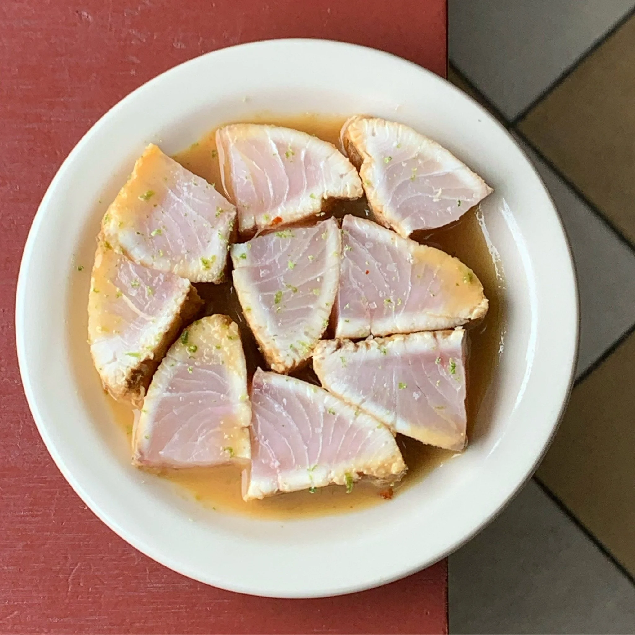 Slices of raw fish in a bowl with sauce and lime zest.