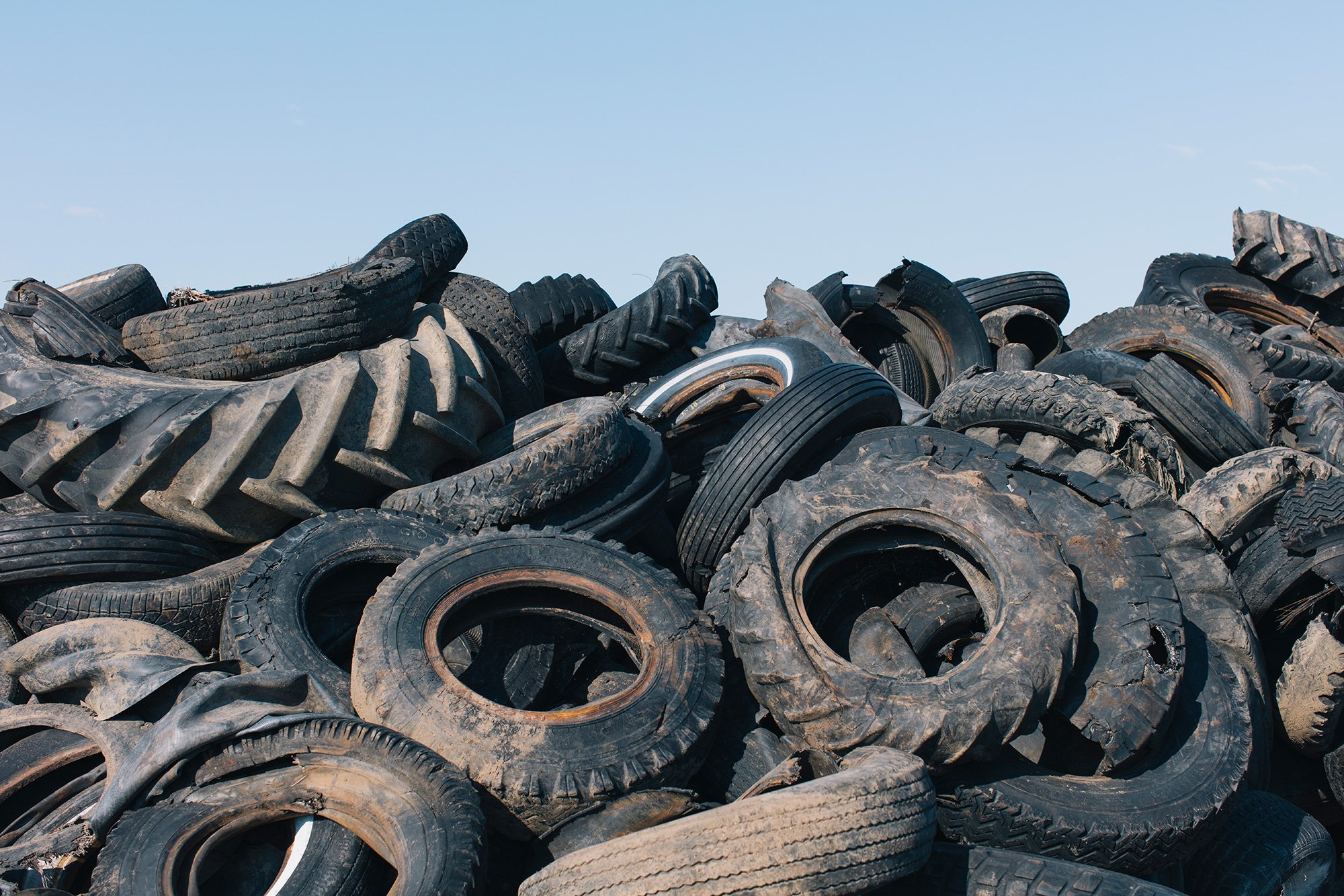 Montón de llantas usadas apiladas con cielo despejado en el fondo.