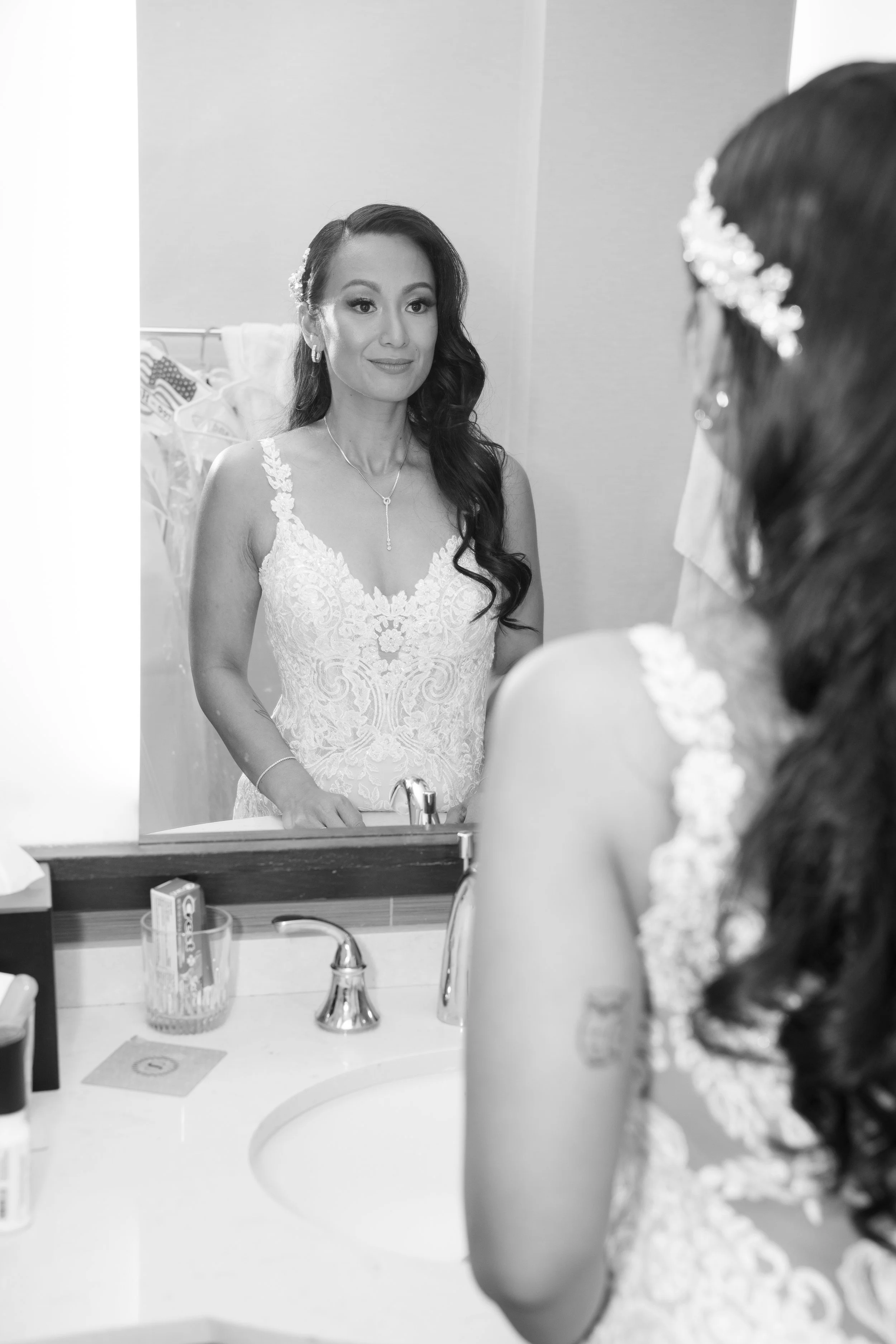 Bride in lace wedding dress looking in mirror, preparing for wedding ceremony.