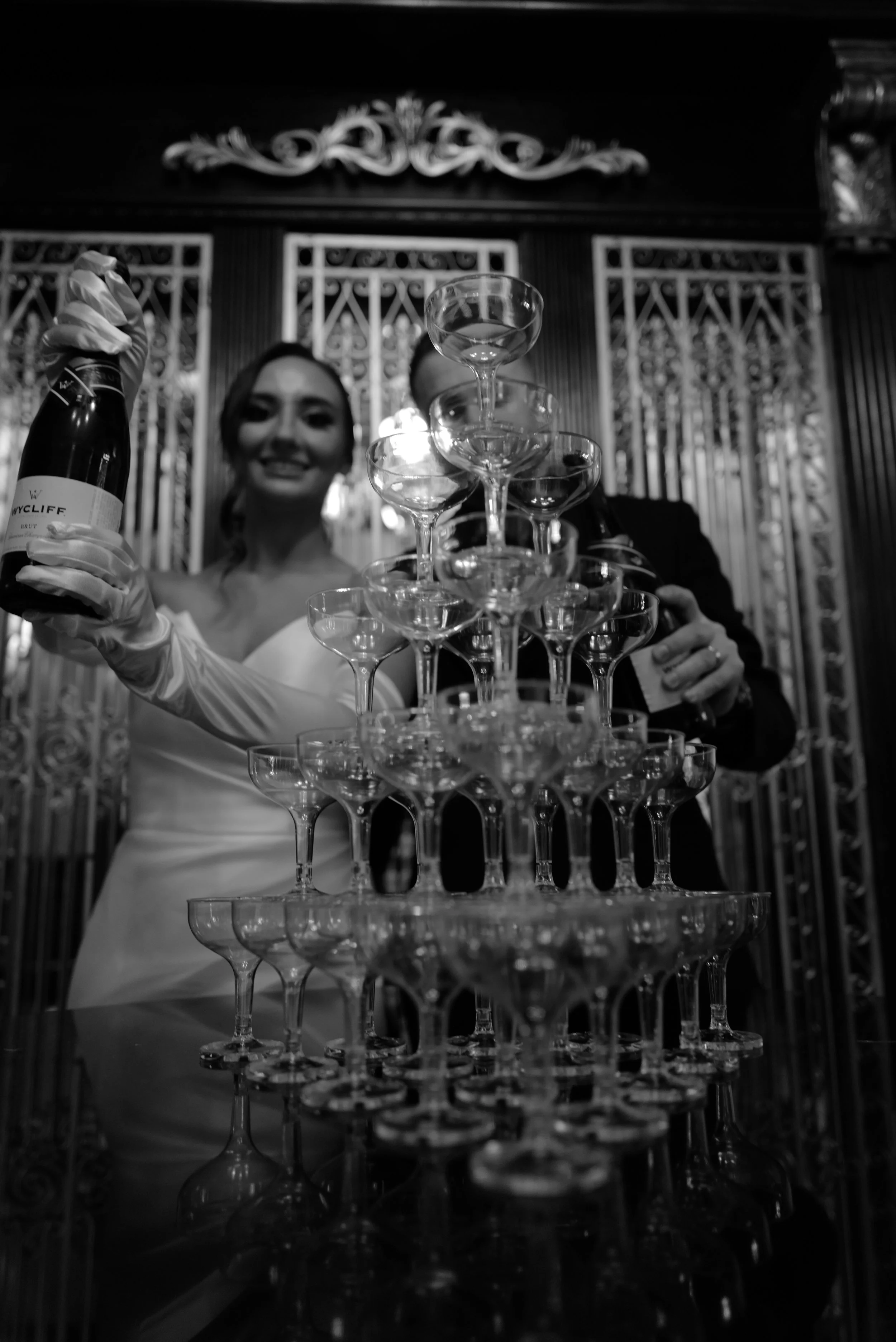 Couple pouring champagne into a pyramid of glasses at a wedding.