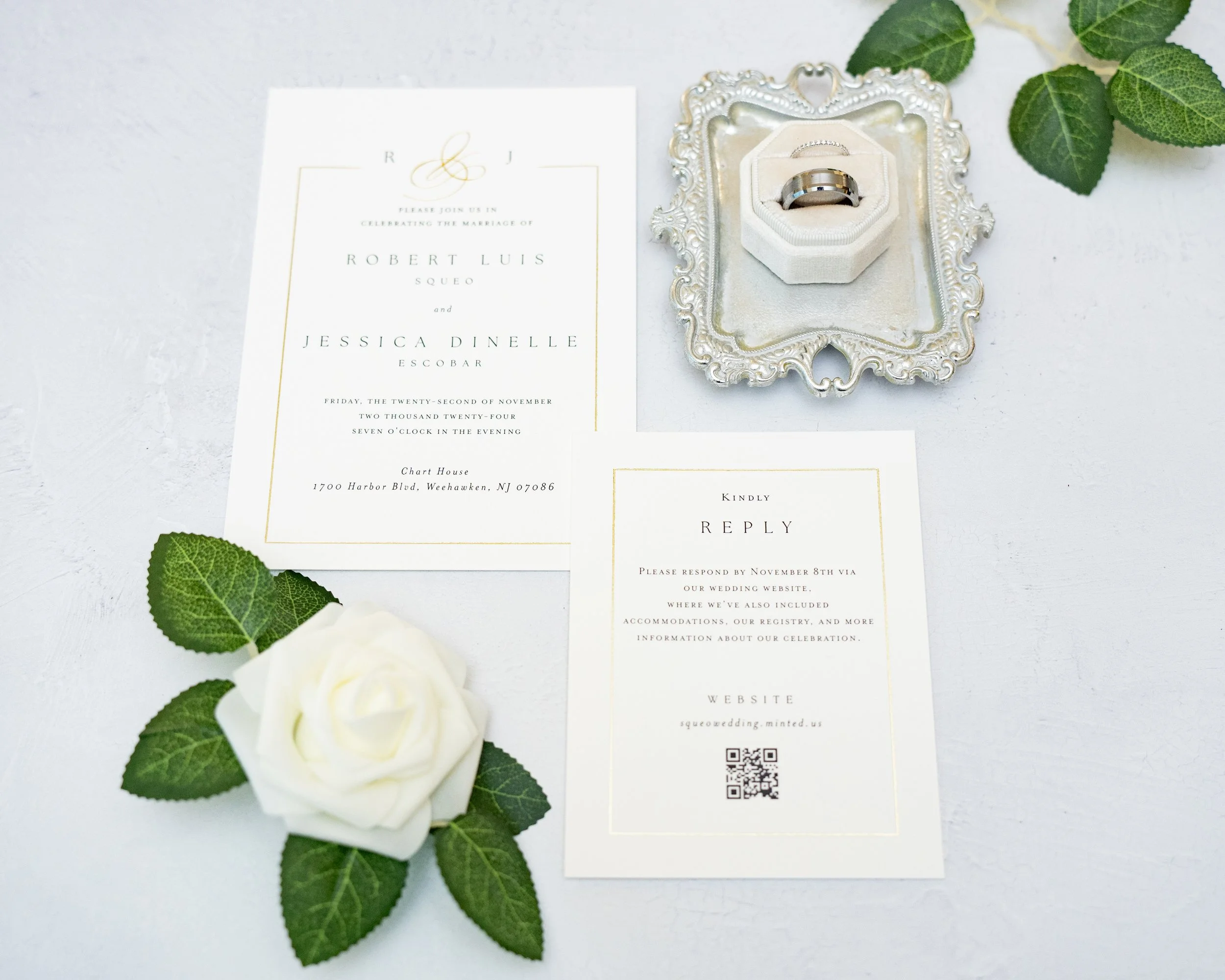 Wedding invitation set with cards, rings in decorative box, white rose, green leaves on light background.