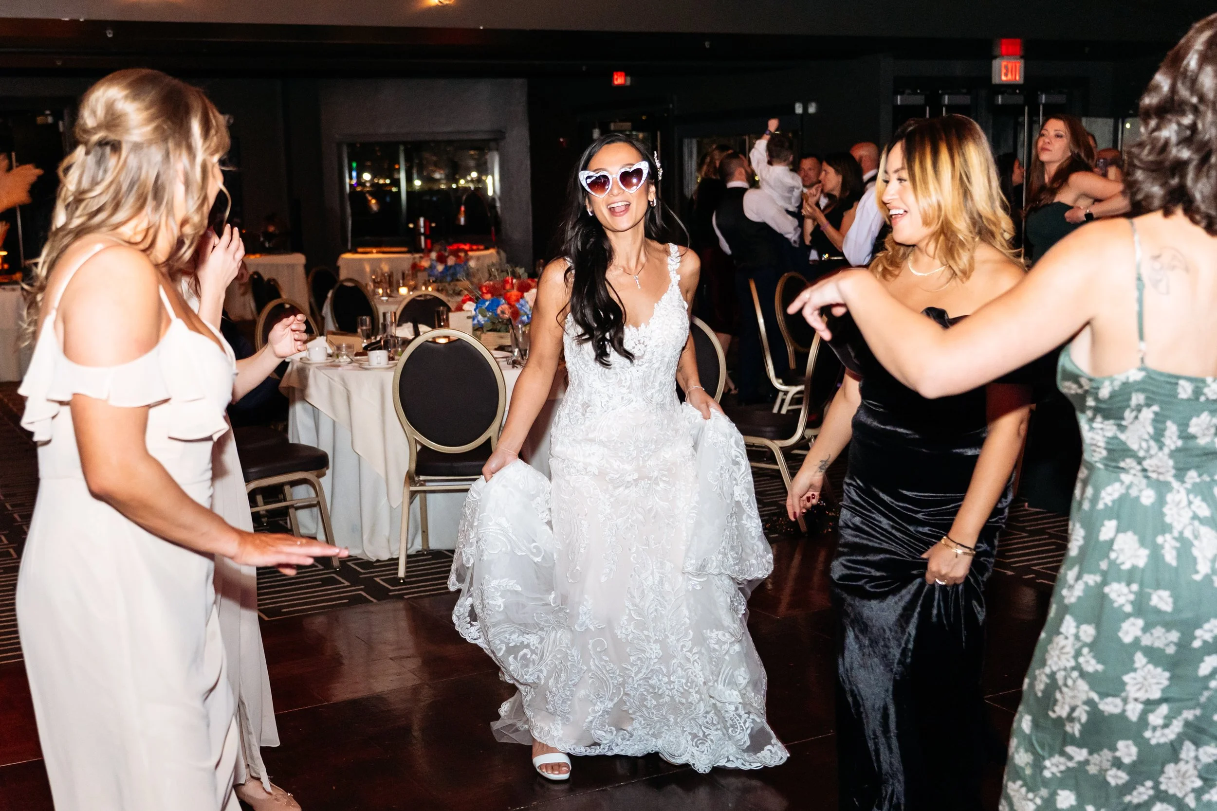 A woman in a wedding dress dancing and smiling with friends at a wedding reception.
