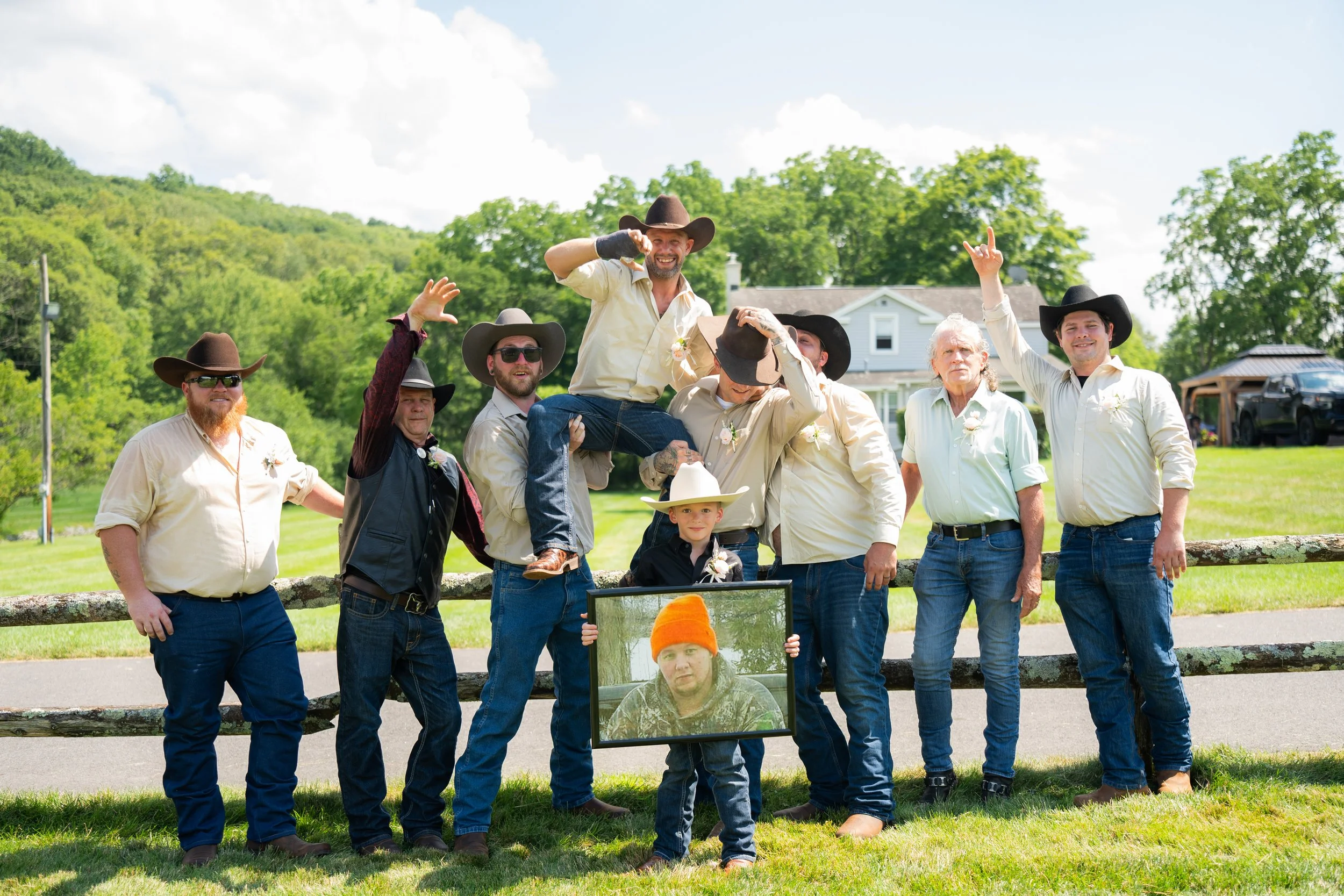 Group of men in cowboy hats posing outdoors with a framed photo of a person.