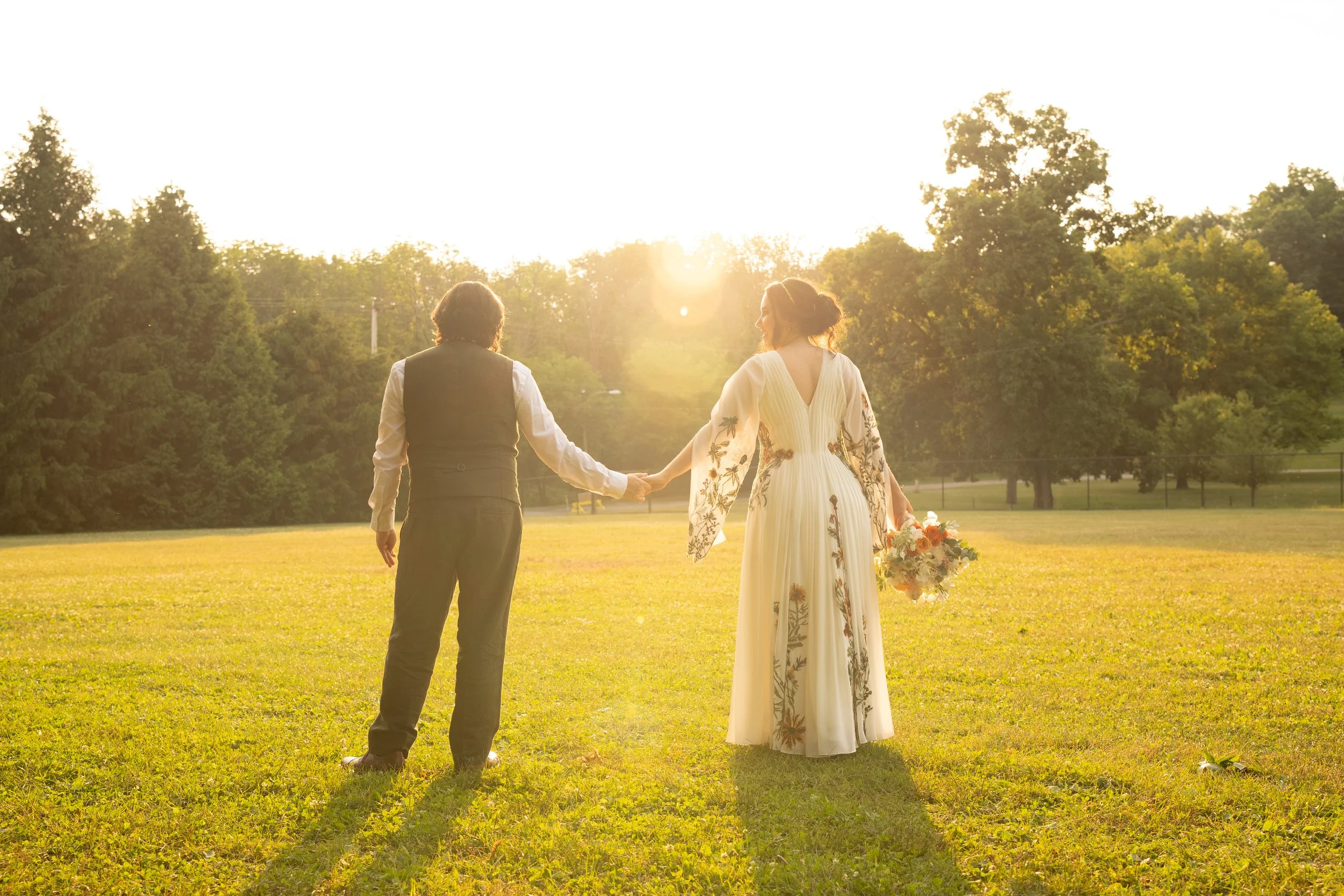 Couple holding hands at outdoor wedding with sunset backdrop