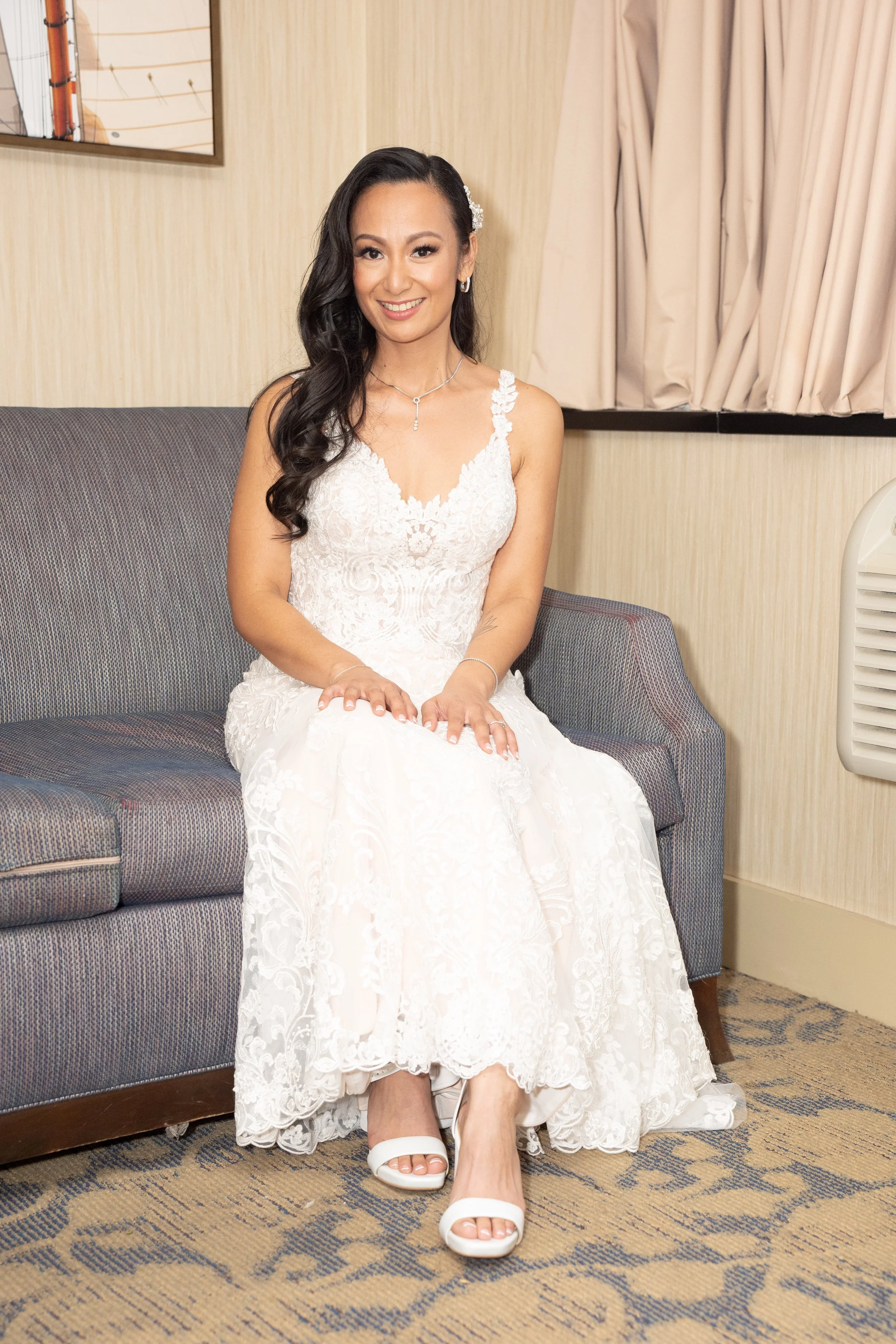 Bride in white lace wedding dress sitting on a couch