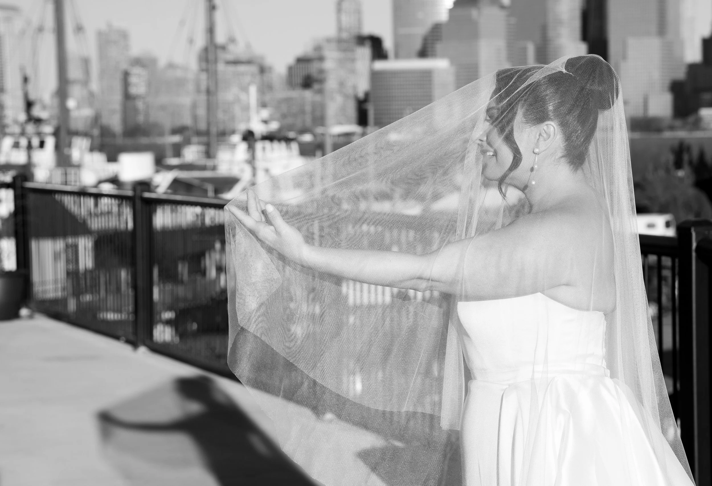 Bride holding veil on urban balcony, black and white photo.
