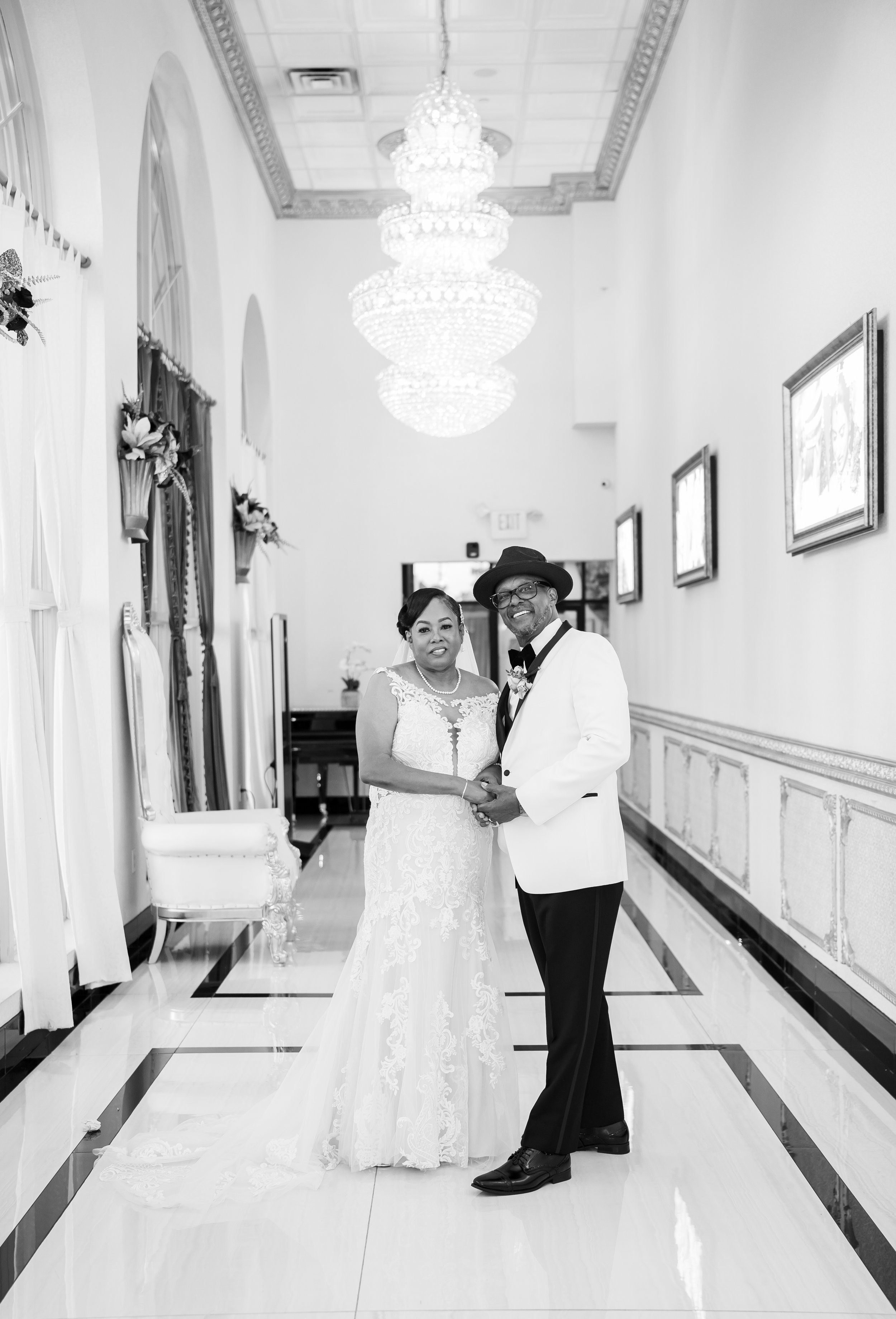 Elegant hallway wedding portrait of a couple in formal attire, chandeliers and artwork in the background.