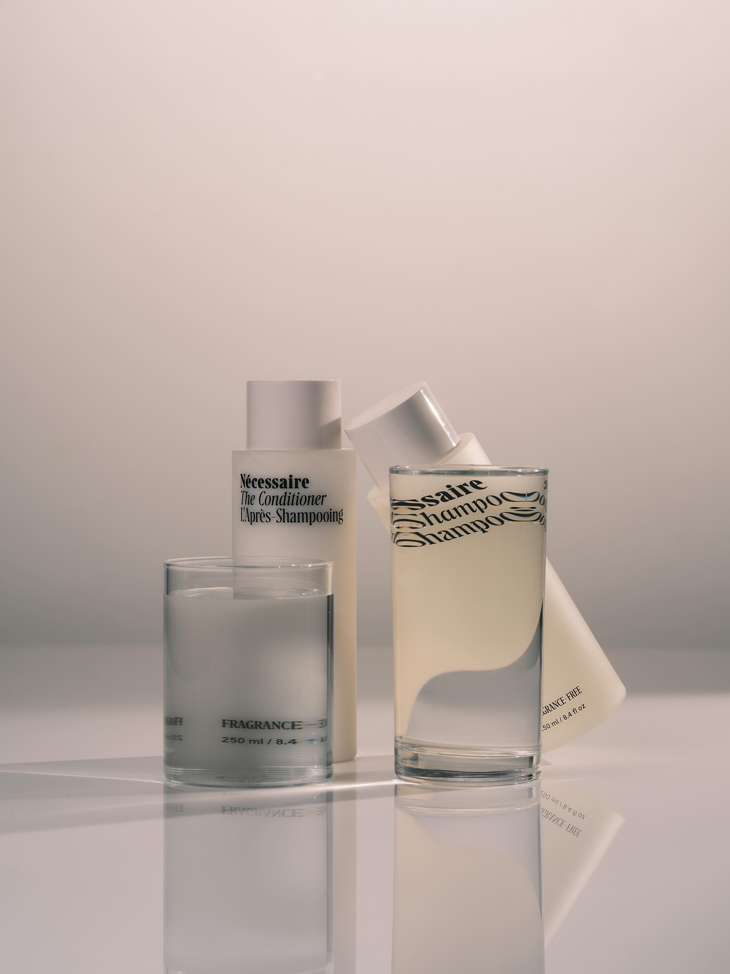 Nécessaire hair care products, including conditioner and shampoo, with minimalistic packaging on a reflective surface.