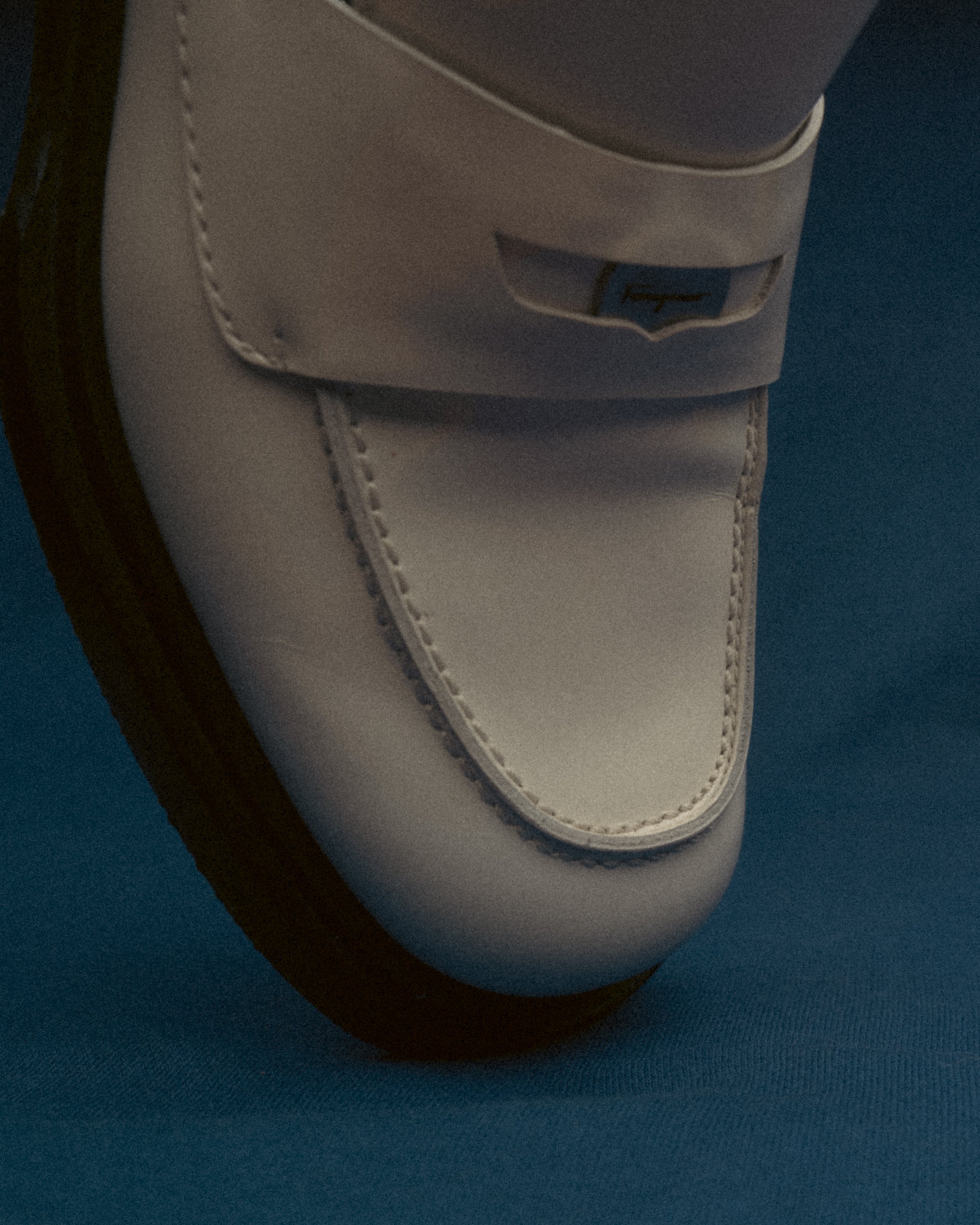 Close-up of a white leather shoe with a branded metal detail on a blue background.