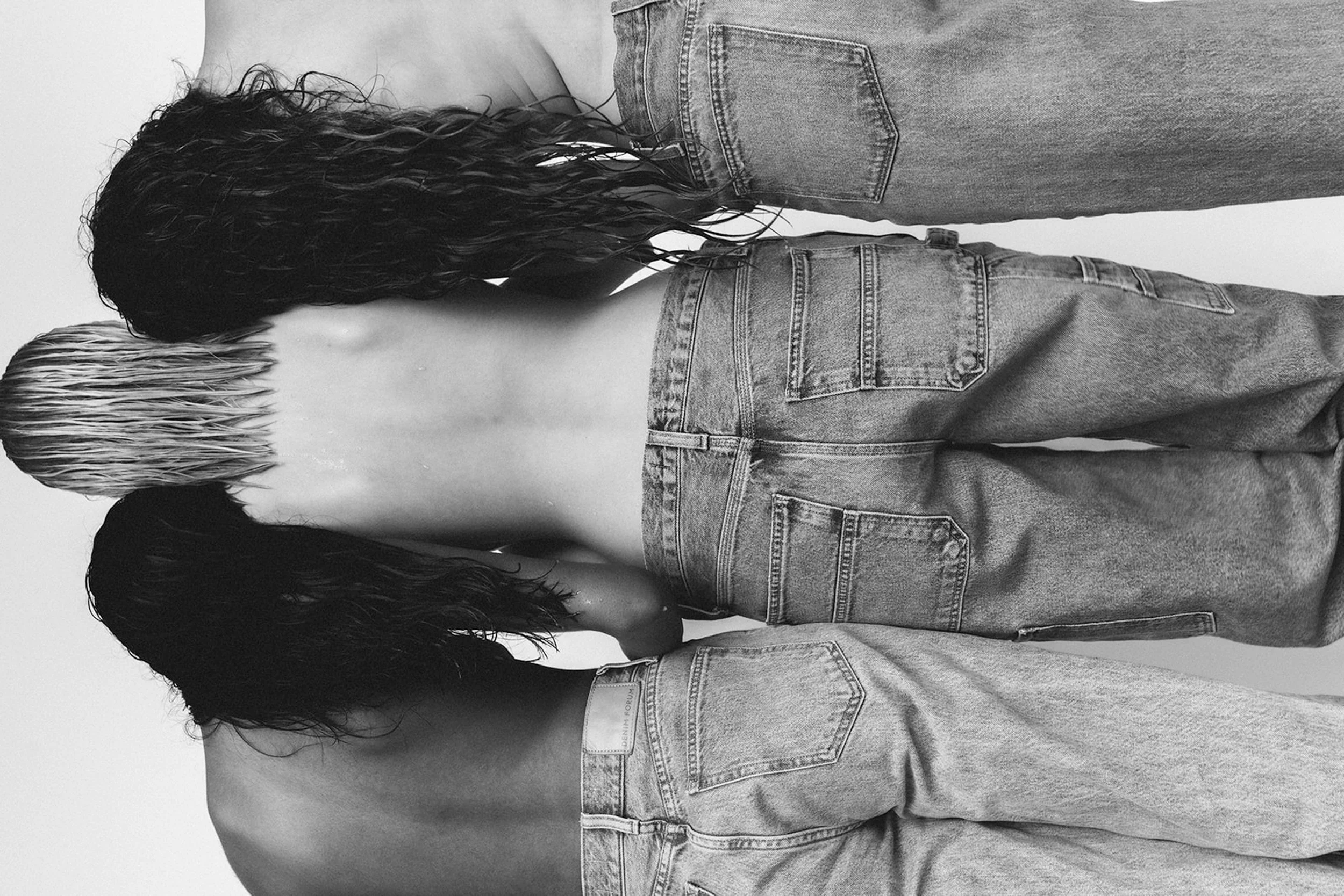 Three women with wet hair and casual denim jeans standing with their backs to the camera.