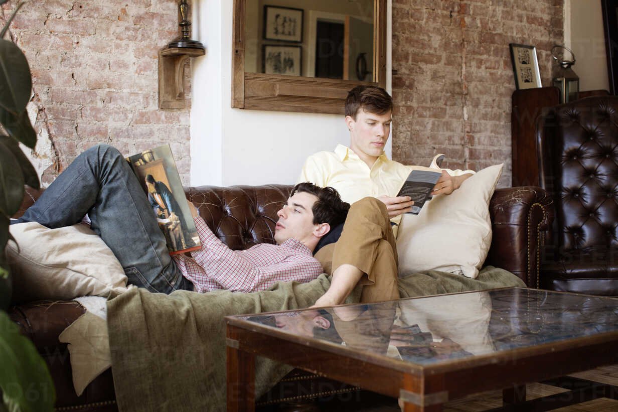 gay-couple-reading-books-while-relaxing-on-sofa-at-home-CAVF35458.jpg