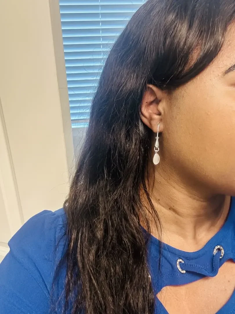 Close-up of a woman's right side showing her wearing a silver earring and a blue shirt, with a background of horizontal window blinds.