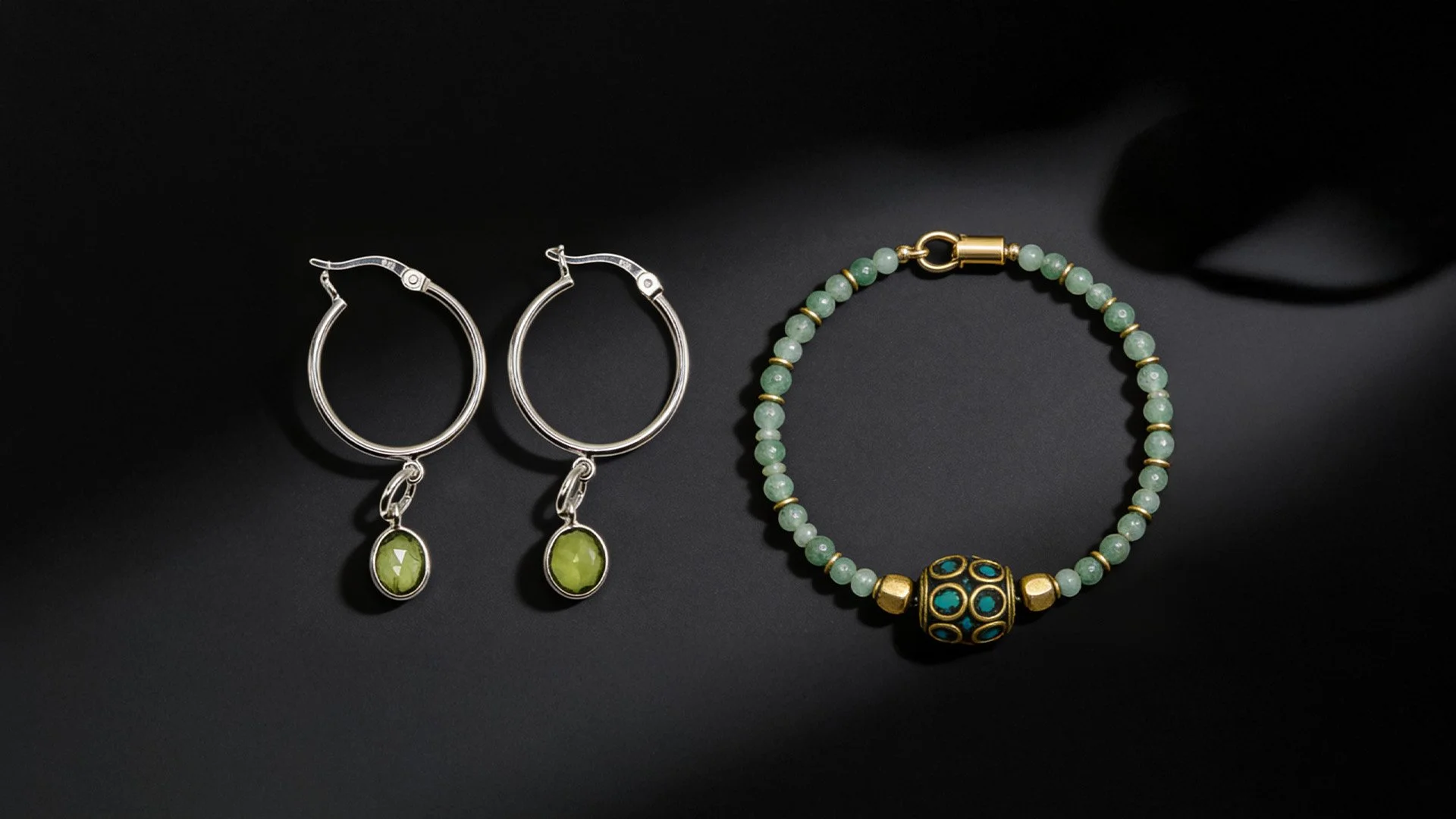 Silver hoop earrings with green gemstone pendants and a beaded necklace with gold and blue accents on a black background.
