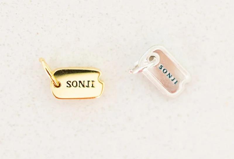 Gold and silver nameplate charms with the name "SONJI" on a white surface.