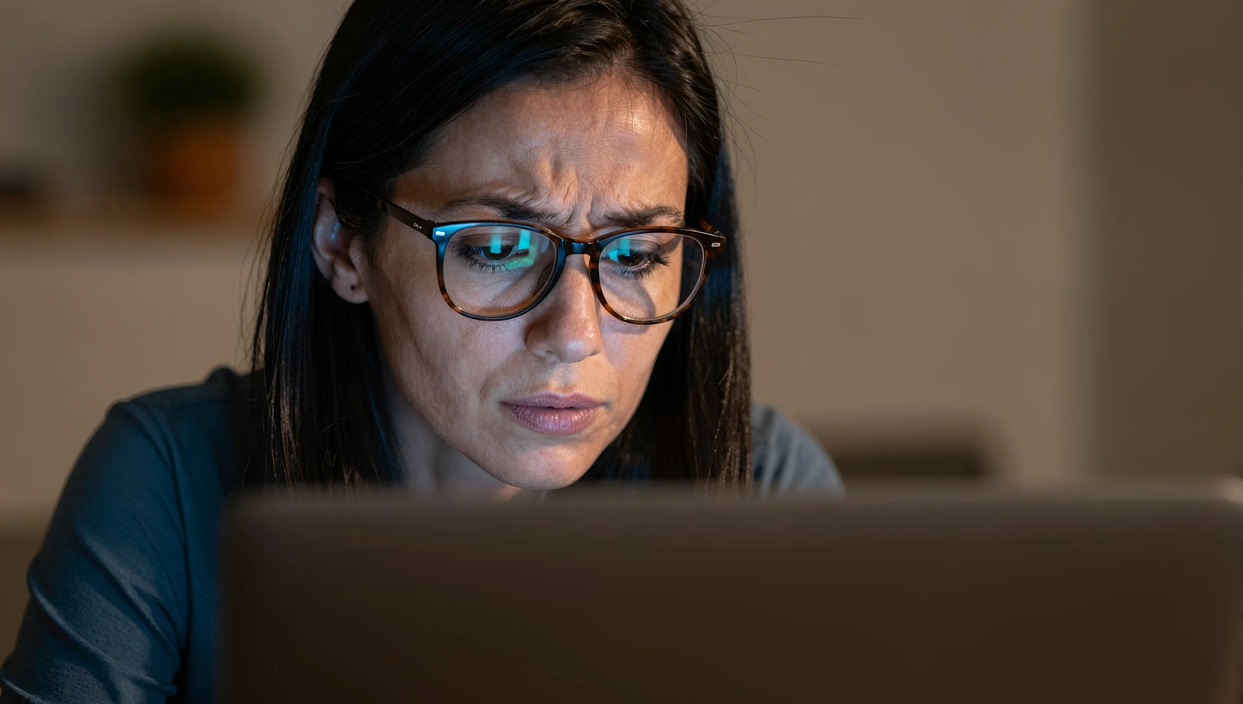 A woman with dark hair and glasses looking at a screen with a serious expression.