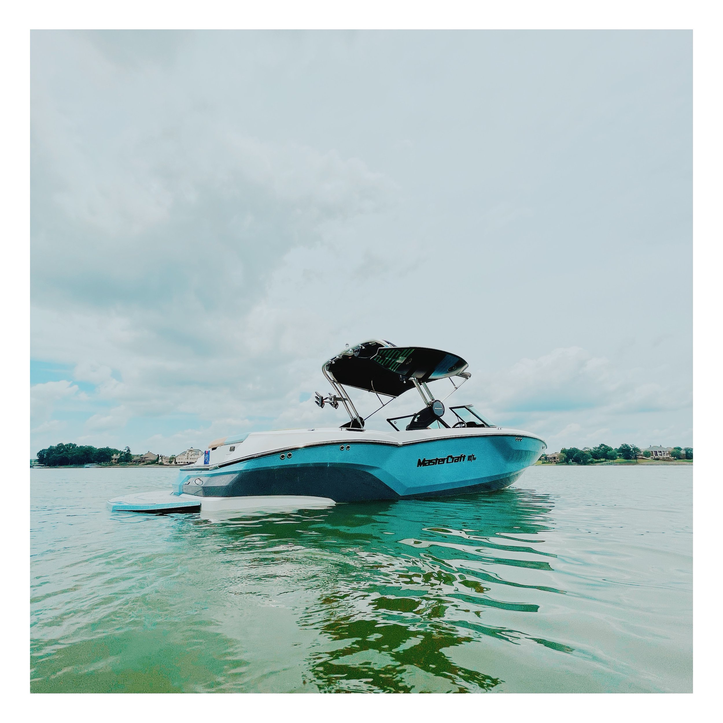 A MasterCraft motorboat with a wakeboard tower floating on a calm lake under cloudy skies.