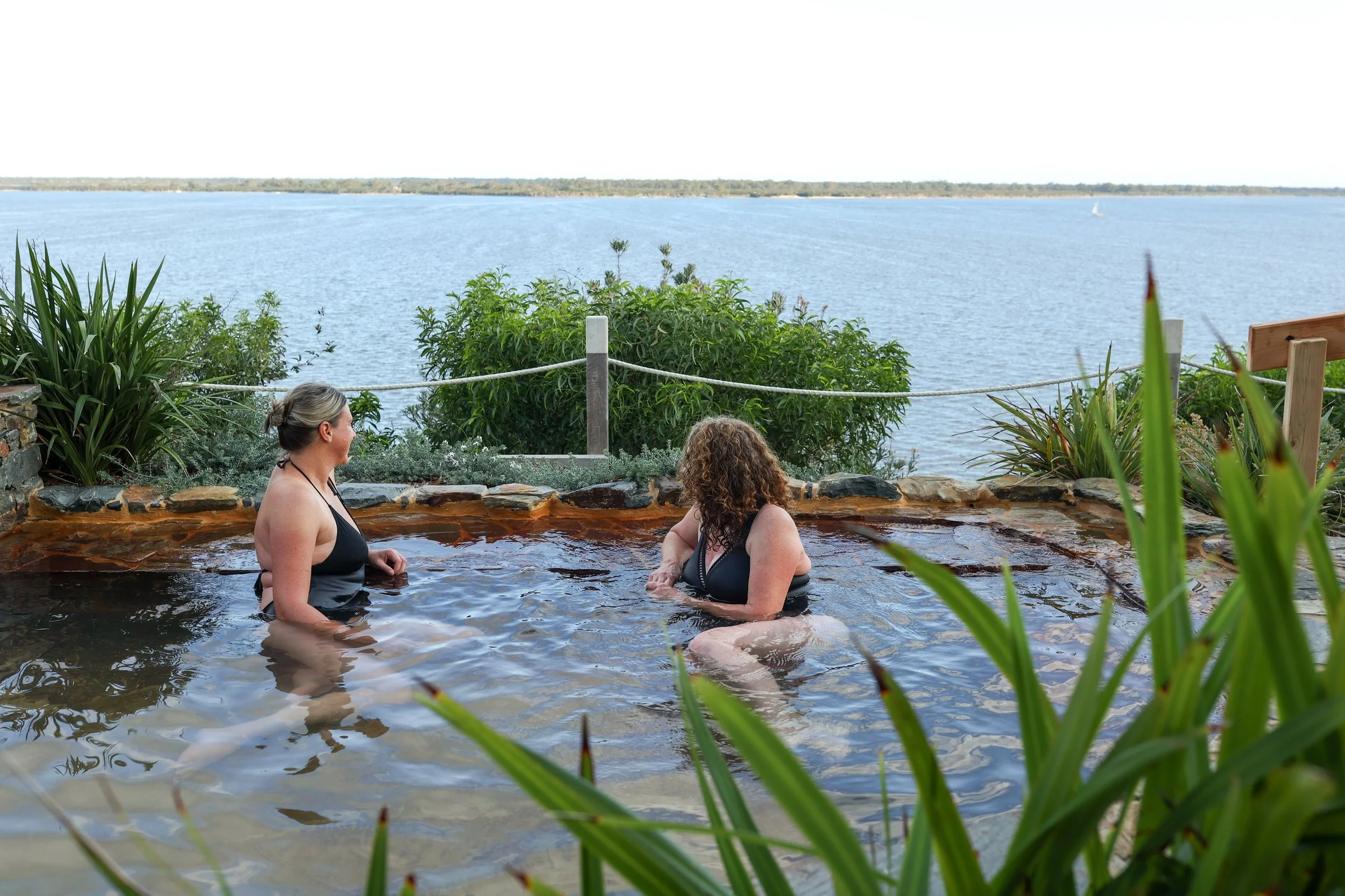 Two women bathing in hot springs overlooking a water view
