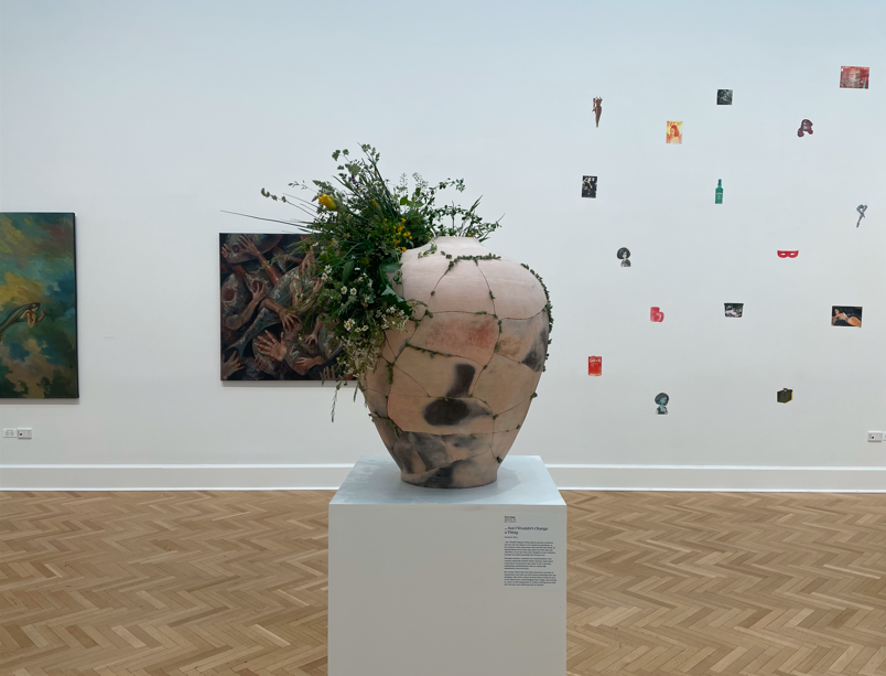 A photo of the centerpiece pot. The pot was fired in a saggar firing and put back together by many hands. In installation, flora were added into the cracks and wounds of the vessel.