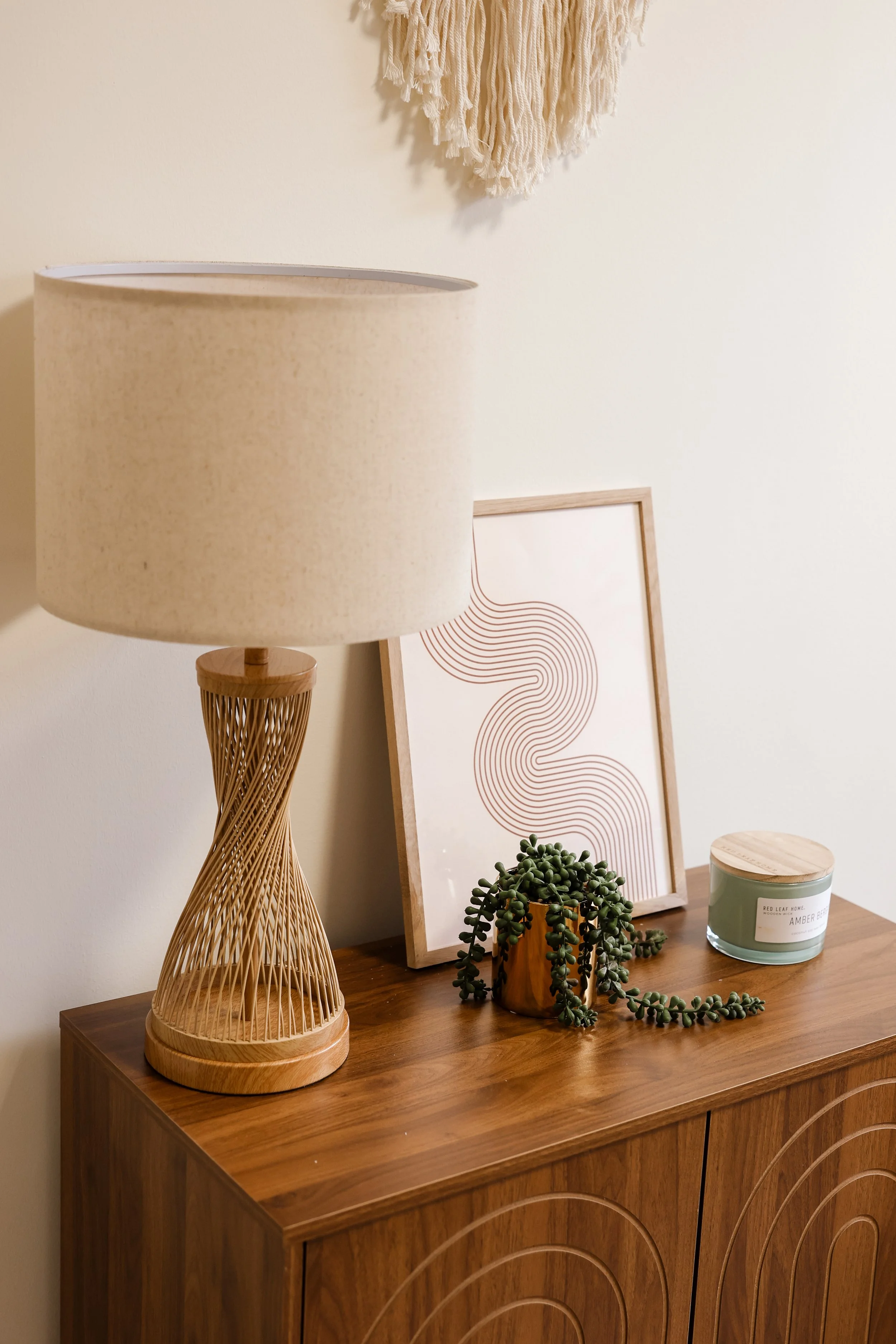 A wooden sideboard with a table lamp, plant, framed artwork, and candle on top in a modern therapist's office