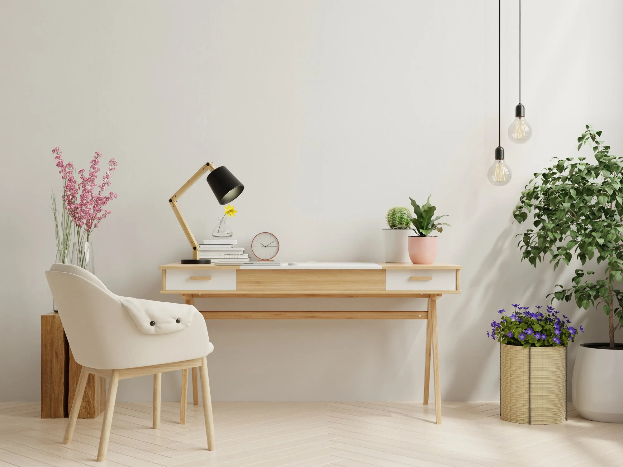 Modern minimalist therapist's office with a white desk, white and wood chair, potted plants, a black adjustable desk lamp, a stack of books, a small clock, and hanging light bulbs.